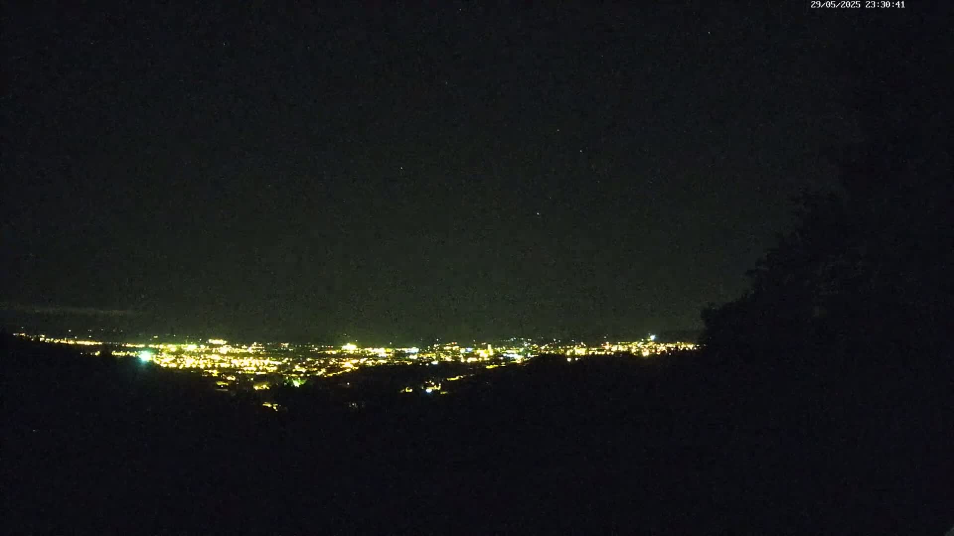 A nighttime view from an elevated position shows a distant city illuminated with many small lights under a clear, starry sky.