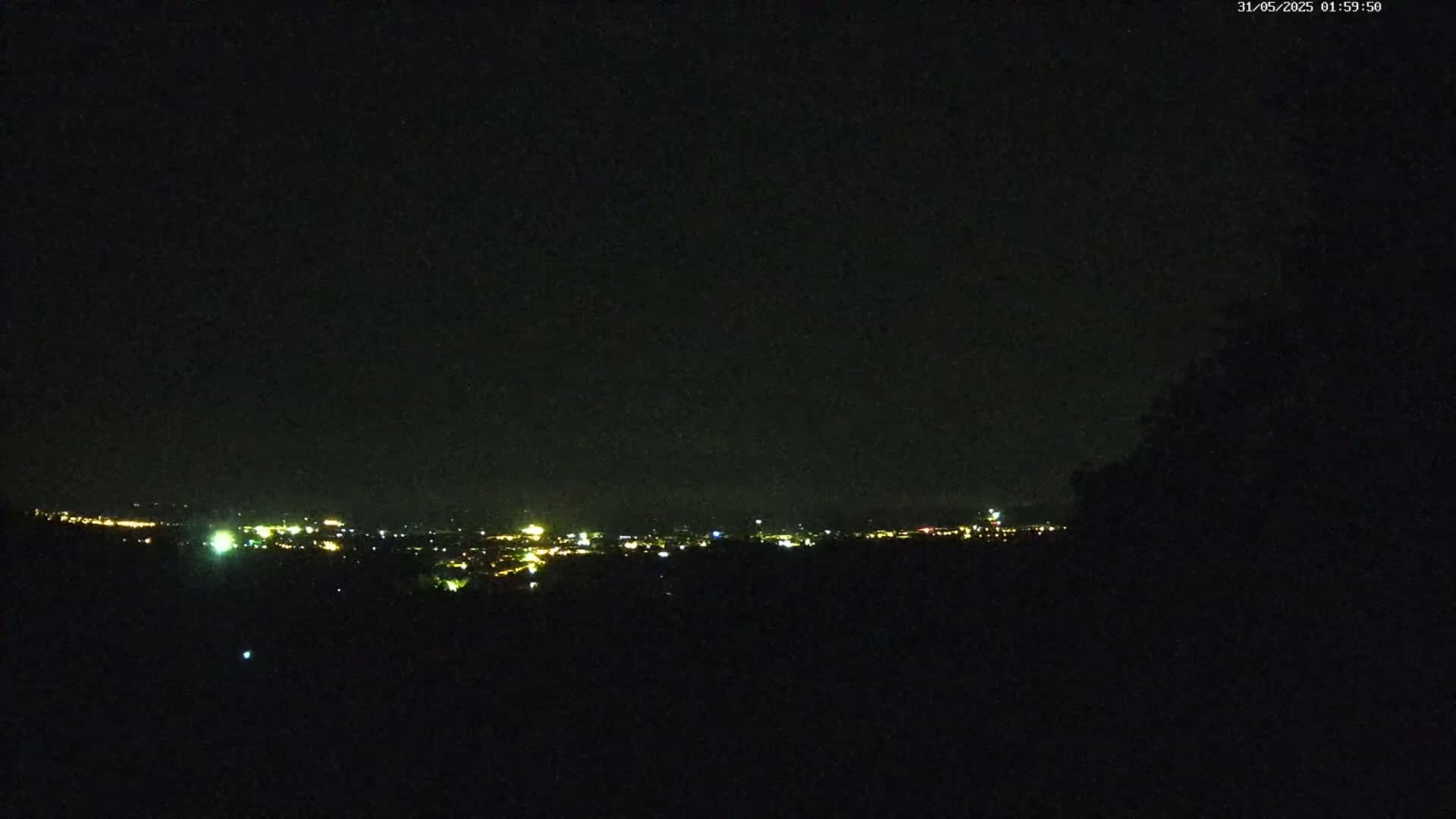 A nighttime view of a city skyline, dimly lit, under a dark, clear sky.