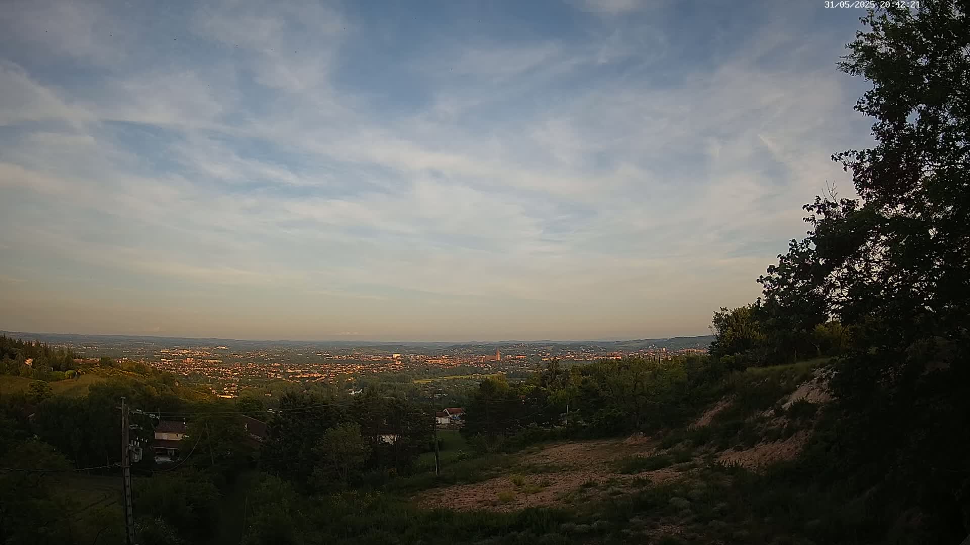 A hilly, wooded area overlooks a sprawling city at sunset under a mostly clear sky.