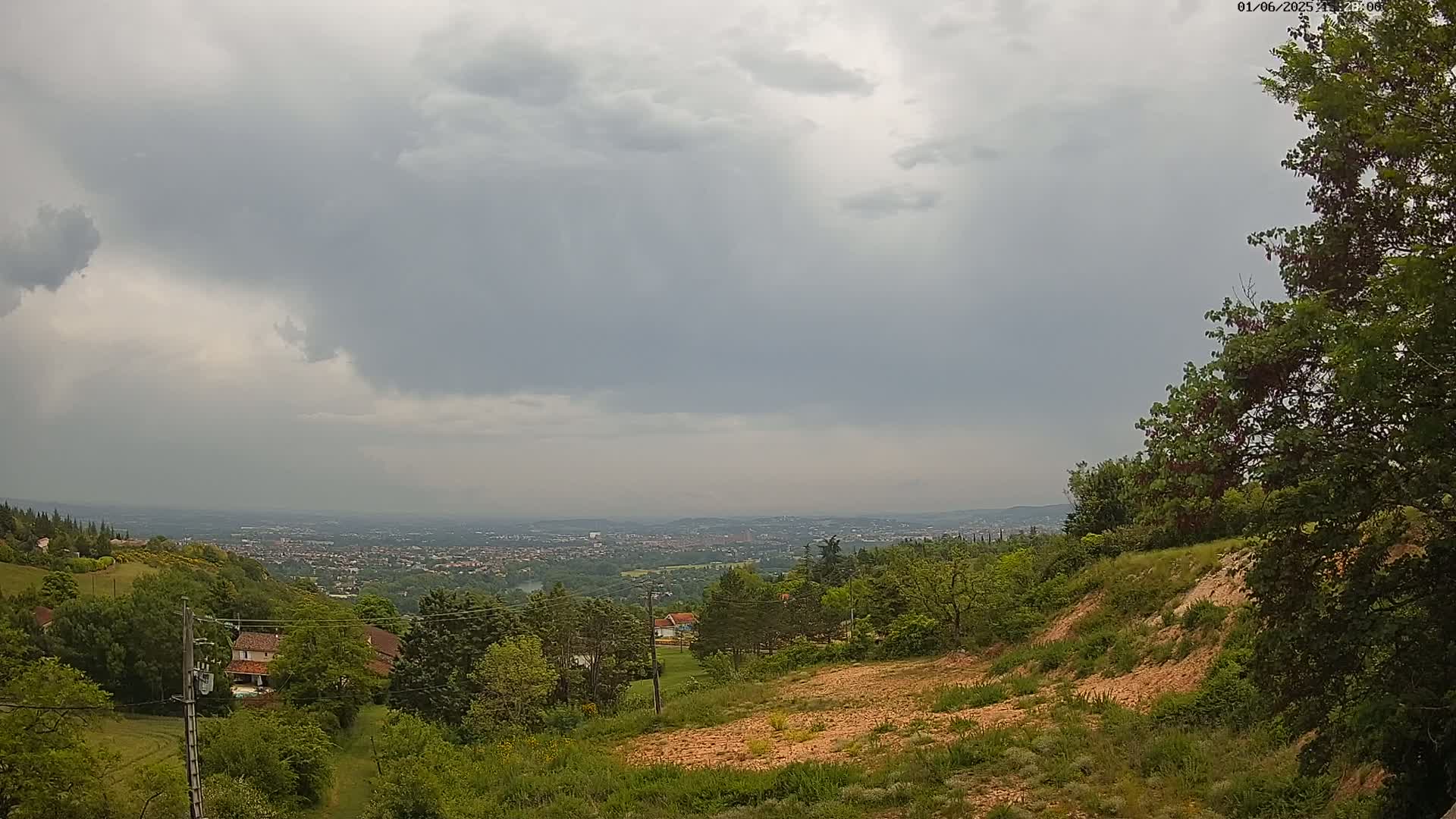 A hilly landscape with lush green vegetation overlooks a distant city under a cloudy, overcast sky.