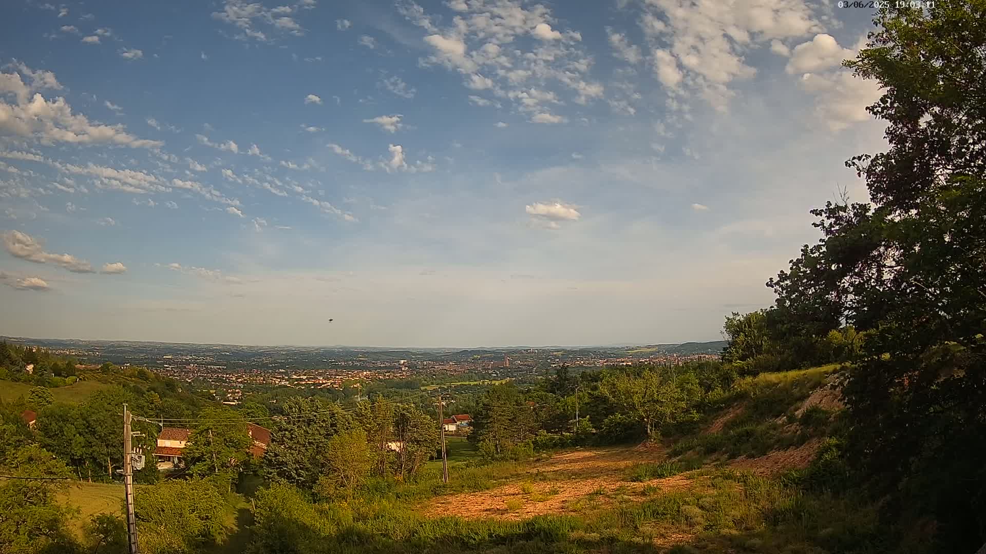 A hillside overlooking a sprawling city under a partly cloudy sky.