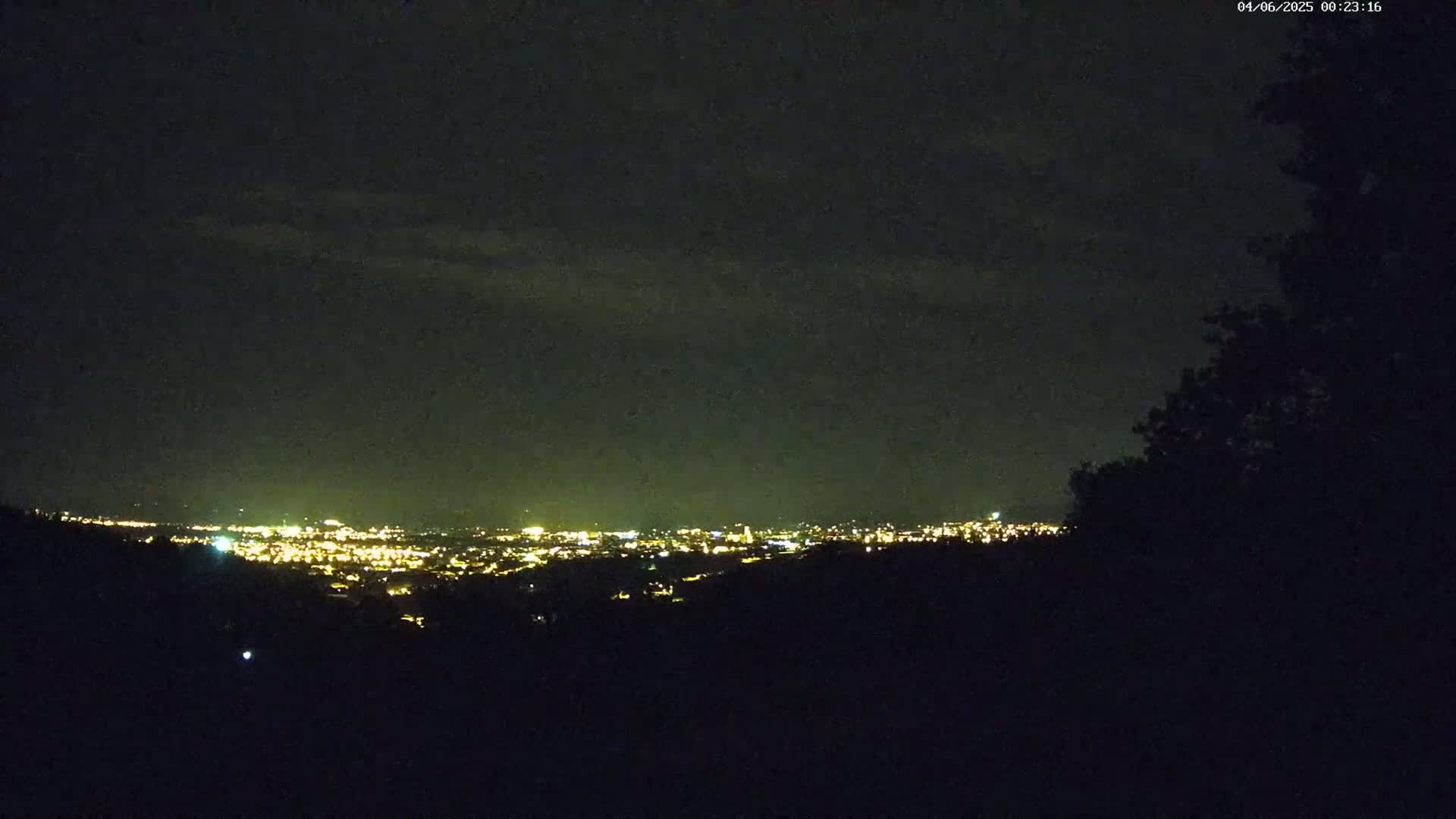 A nighttime view of a distant city illuminated by lights under a dark, cloudy sky.