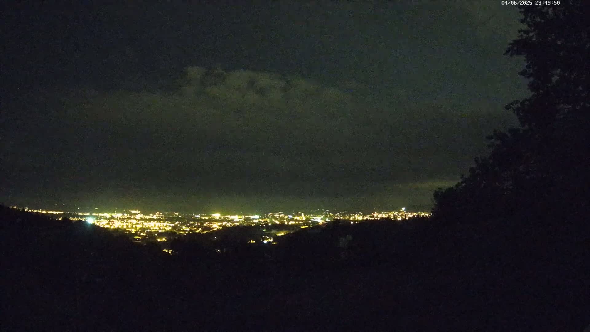 A nighttime view shows a distant city glowing with lights under a dark, cloudy sky.