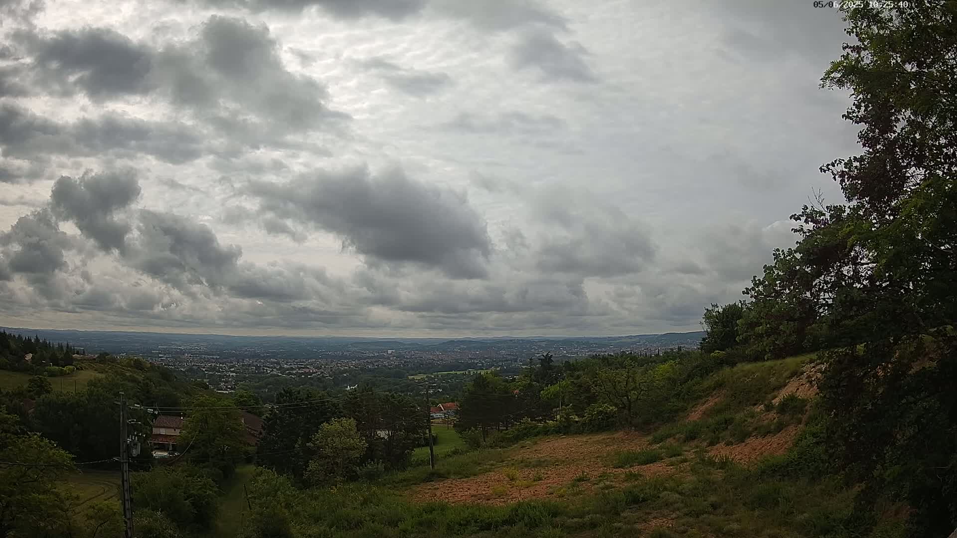 A hilly, green landscape overlooks a distant city under a cloudy sky.