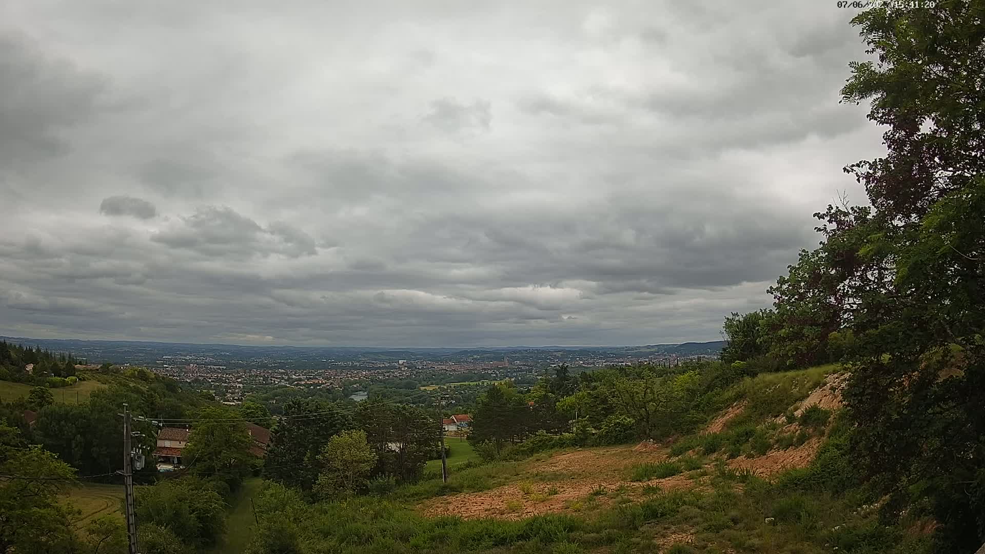 A hilly landscape with overcast skies shows a distant city sprawling beneath a cloudy sky.