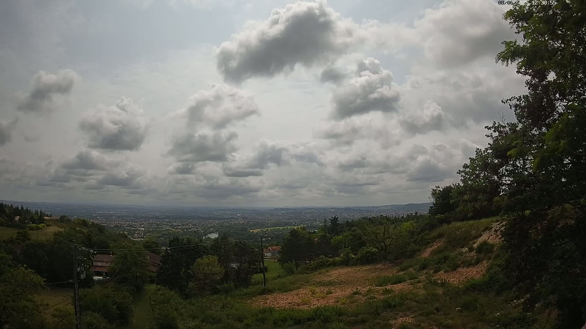 A hilly landscape with lush green vegetation overlooks a distant city under a partly cloudy sky.