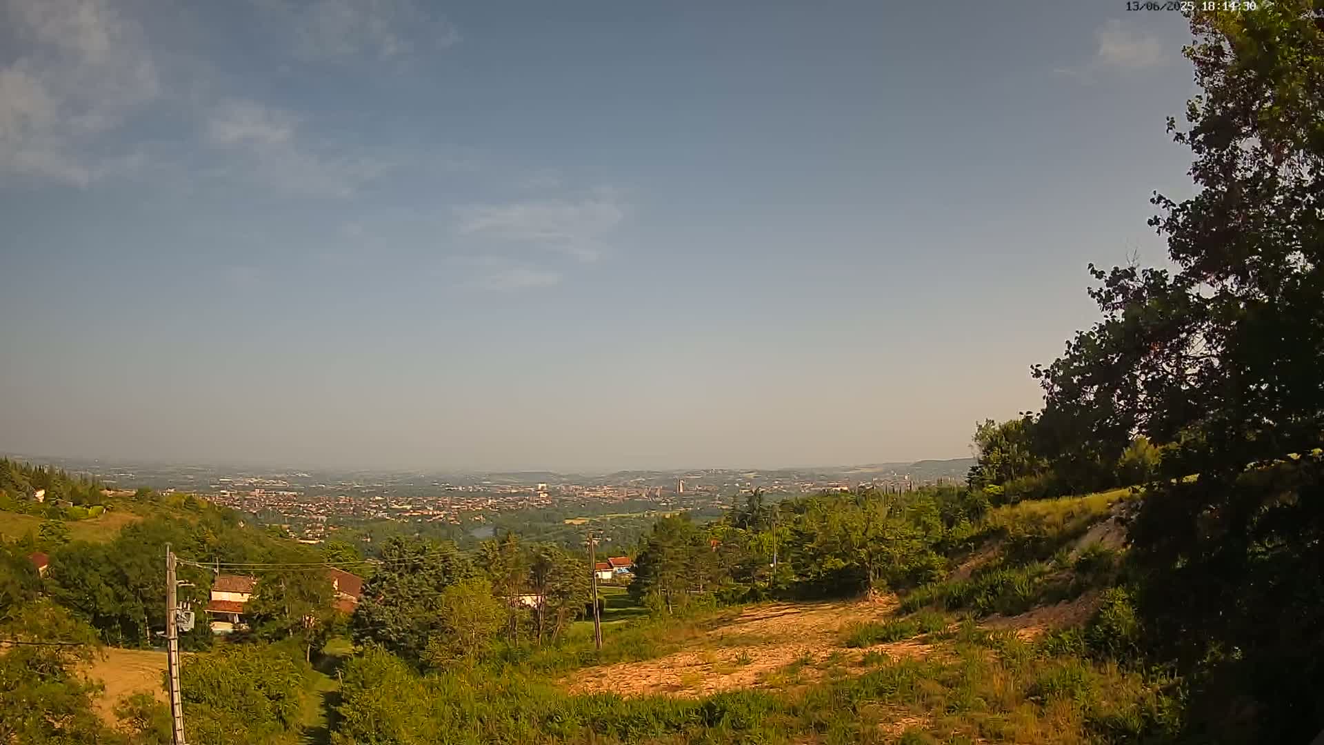 A hillside covered in green vegetation overlooks a hazy, distant city under a mostly clear, light blue sky.