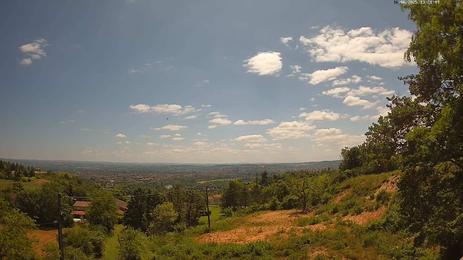 A partly sunny day reveals a sprawling vista of a city nestled in a valley, surrounded by lush green hills and trees.