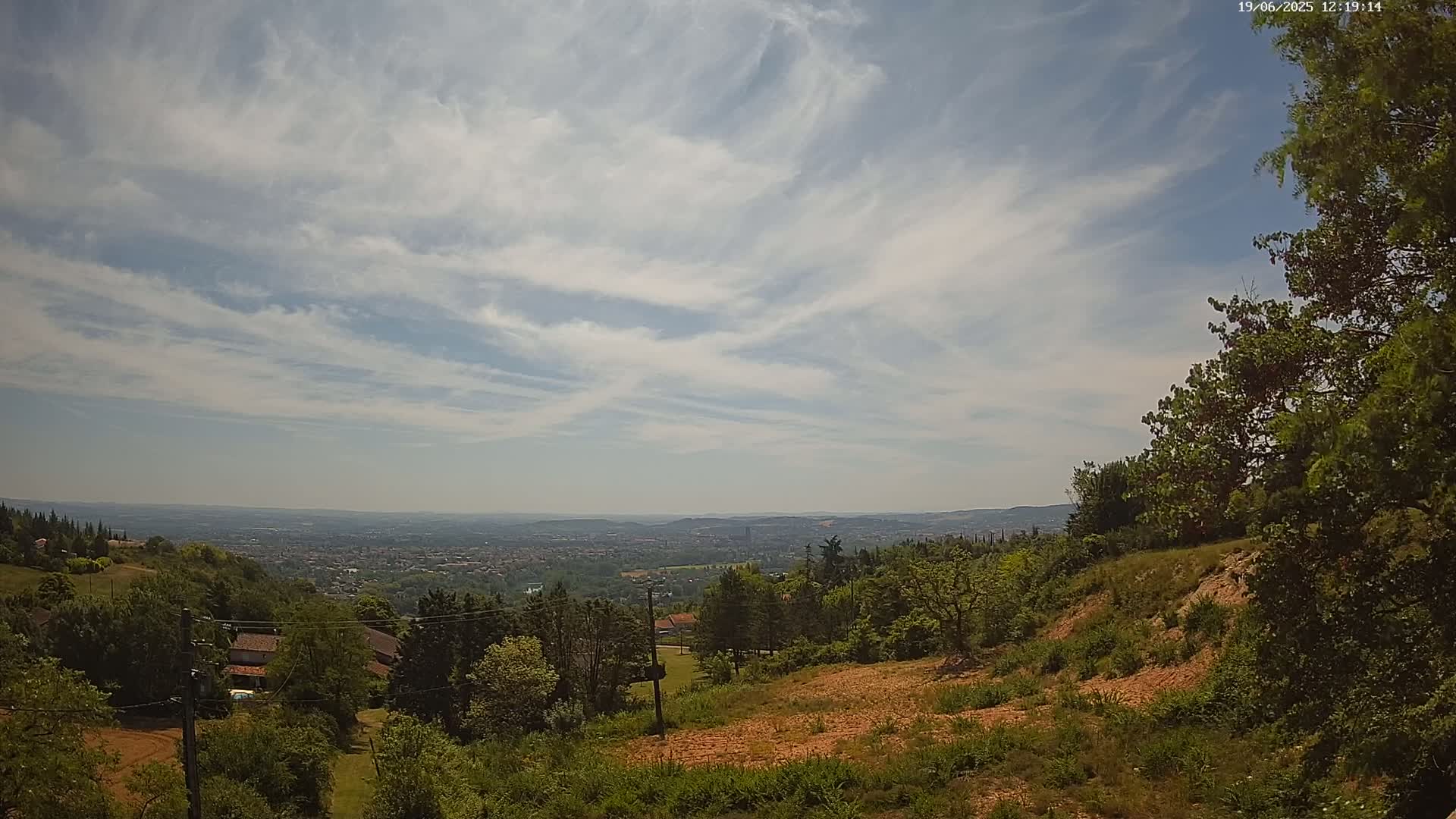 A hilly landscape with green trees and a distant city view under a partly cloudy sky.
