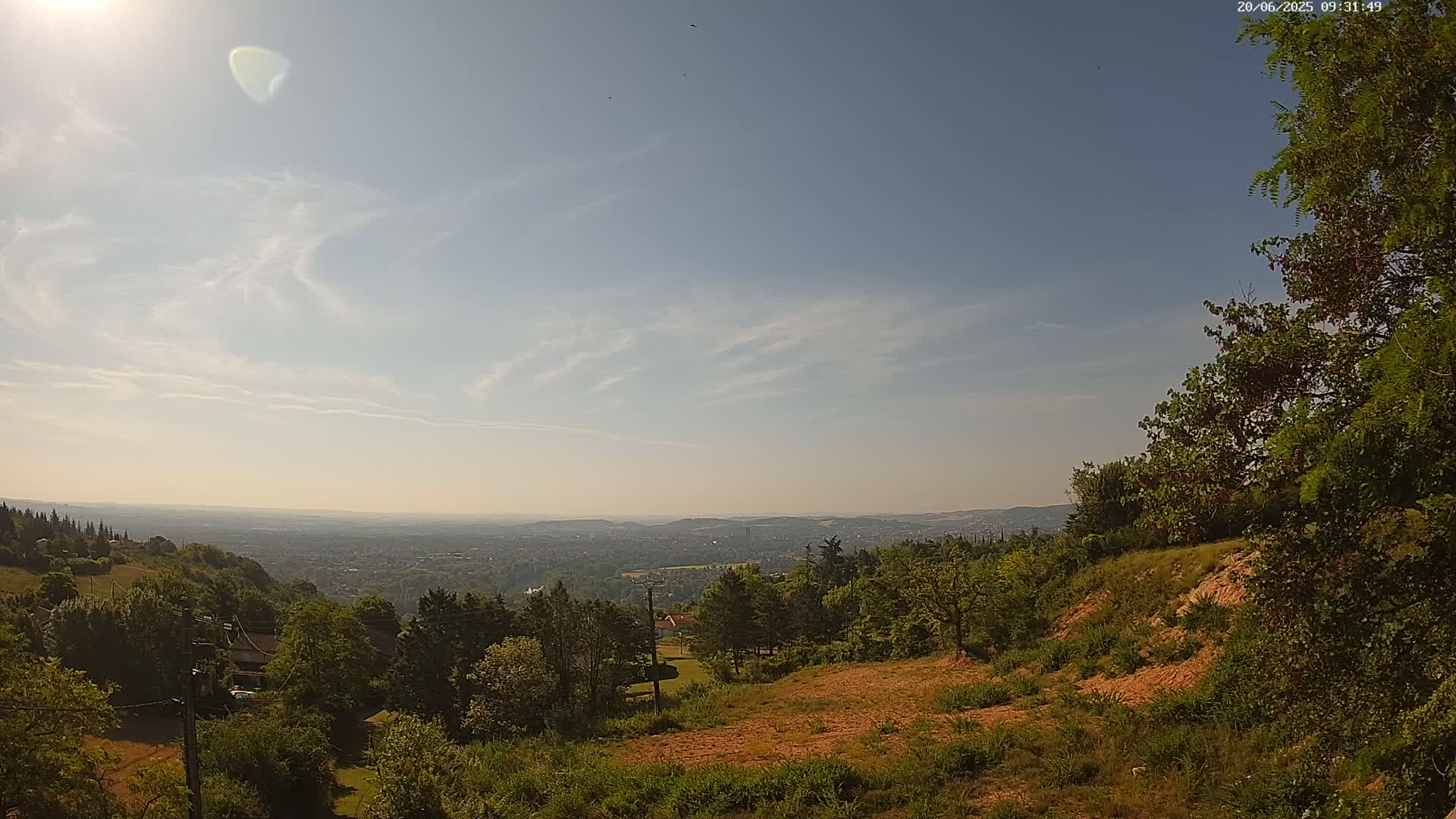A sunny day reveals a panoramic view of a city nestled in a valley surrounded by lush green hills and forests.