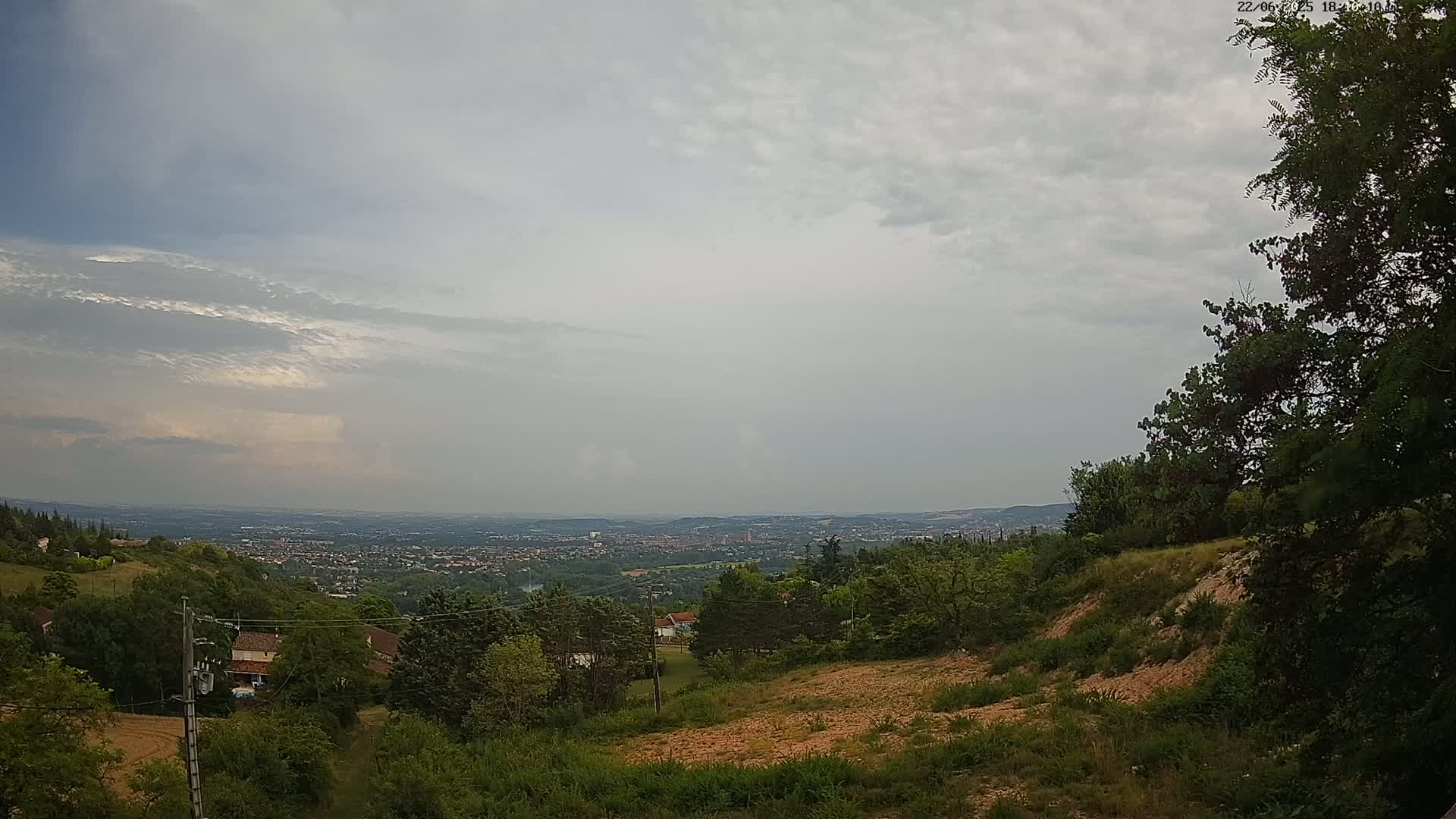 A hilly landscape with a distant view of a city under an overcast sky.