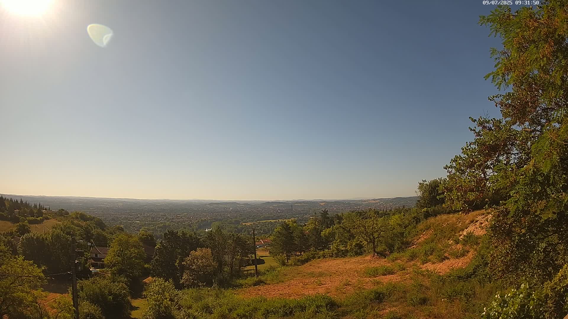 A sunny, expansive view from a hilltop reveals a sprawling cityscape nestled among verdant hills and trees.