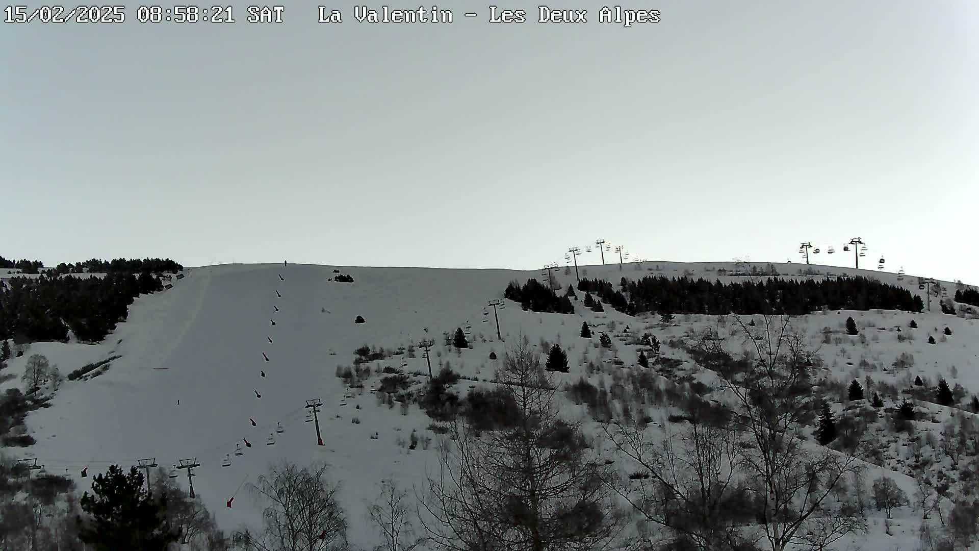 A snow-covered ski slope with several ski lifts and sparsely wooded areas under a pale gray sky.