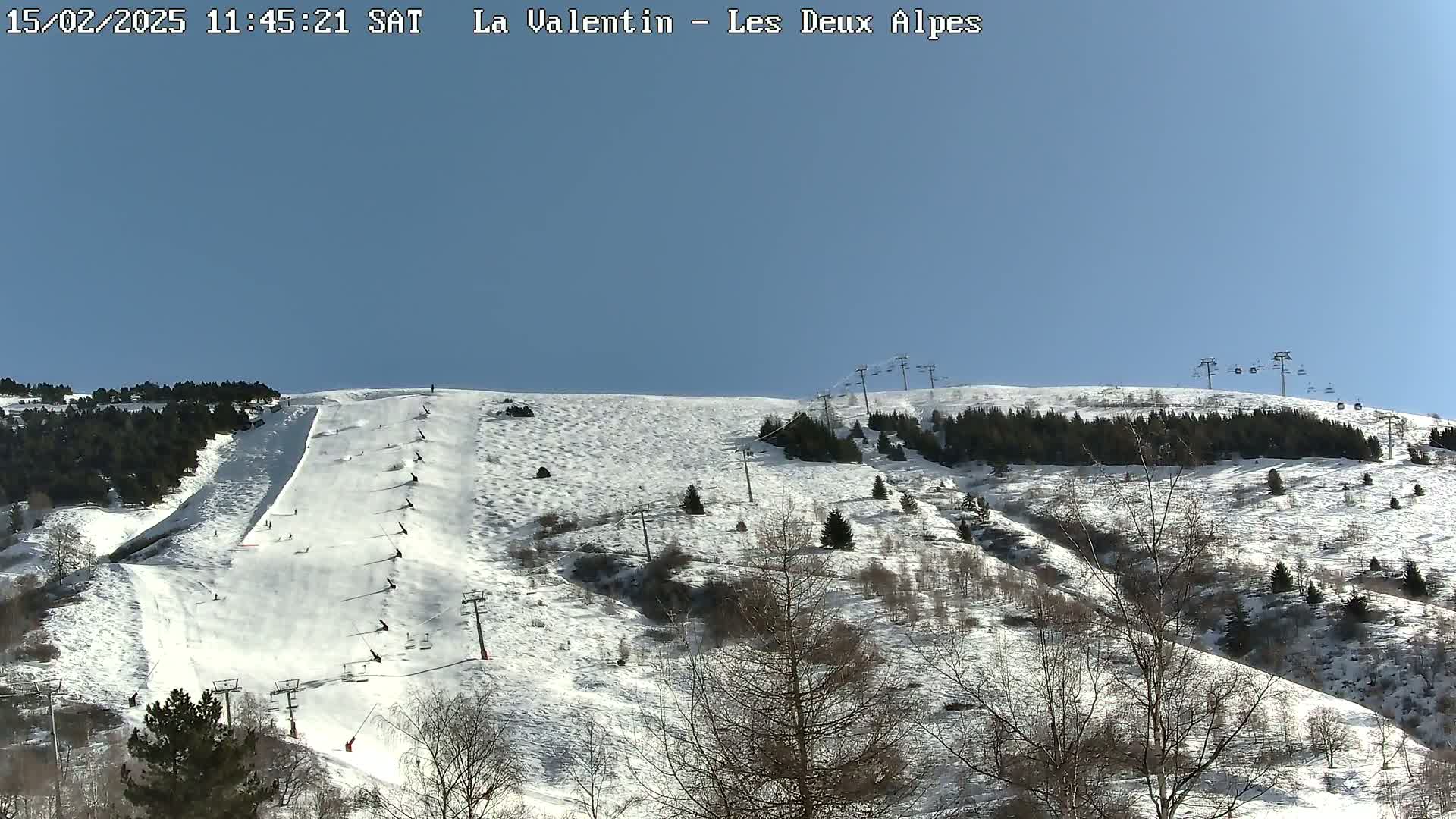 A snow-covered mountain slope with skiers and ski lifts under a clear blue sky.