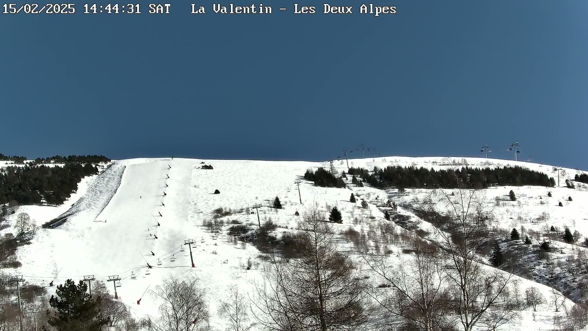 A snow-covered ski slope with several skiers and ski lifts under a clear blue sky.