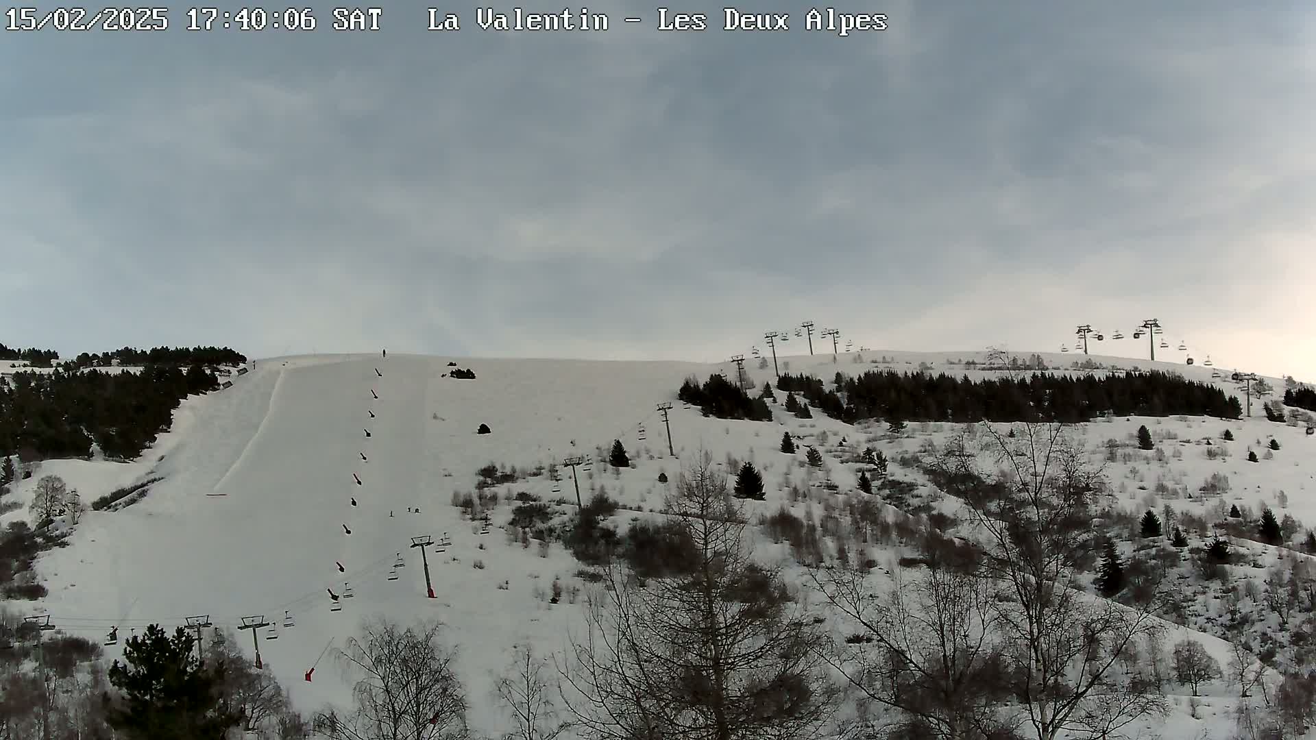 A snow-covered ski slope with several chairlifts and sparsely populated, snow-covered trees under a cloudy sky.