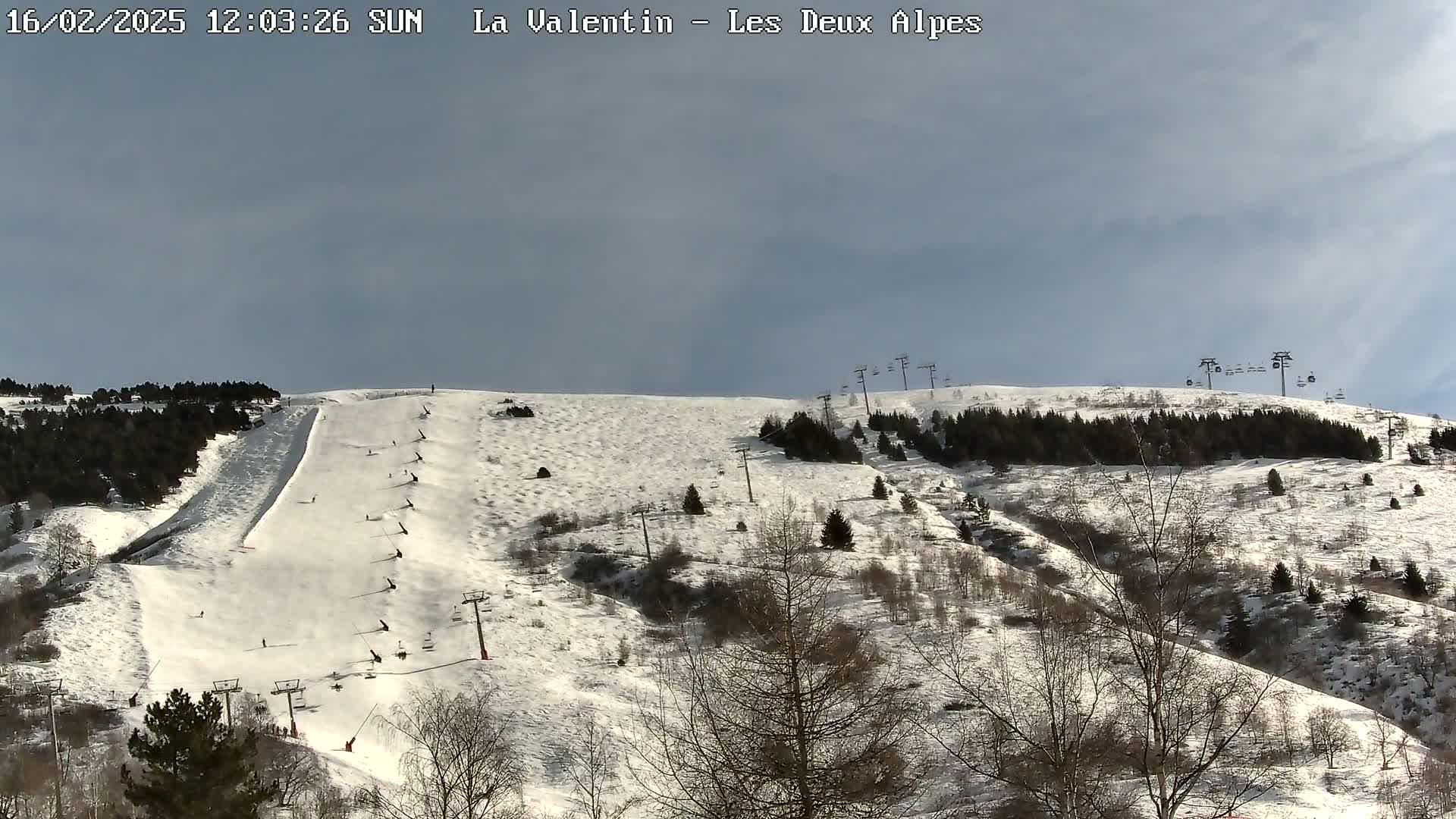 A snow-covered ski slope with several skiers and ski lifts under a mostly sunny sky.