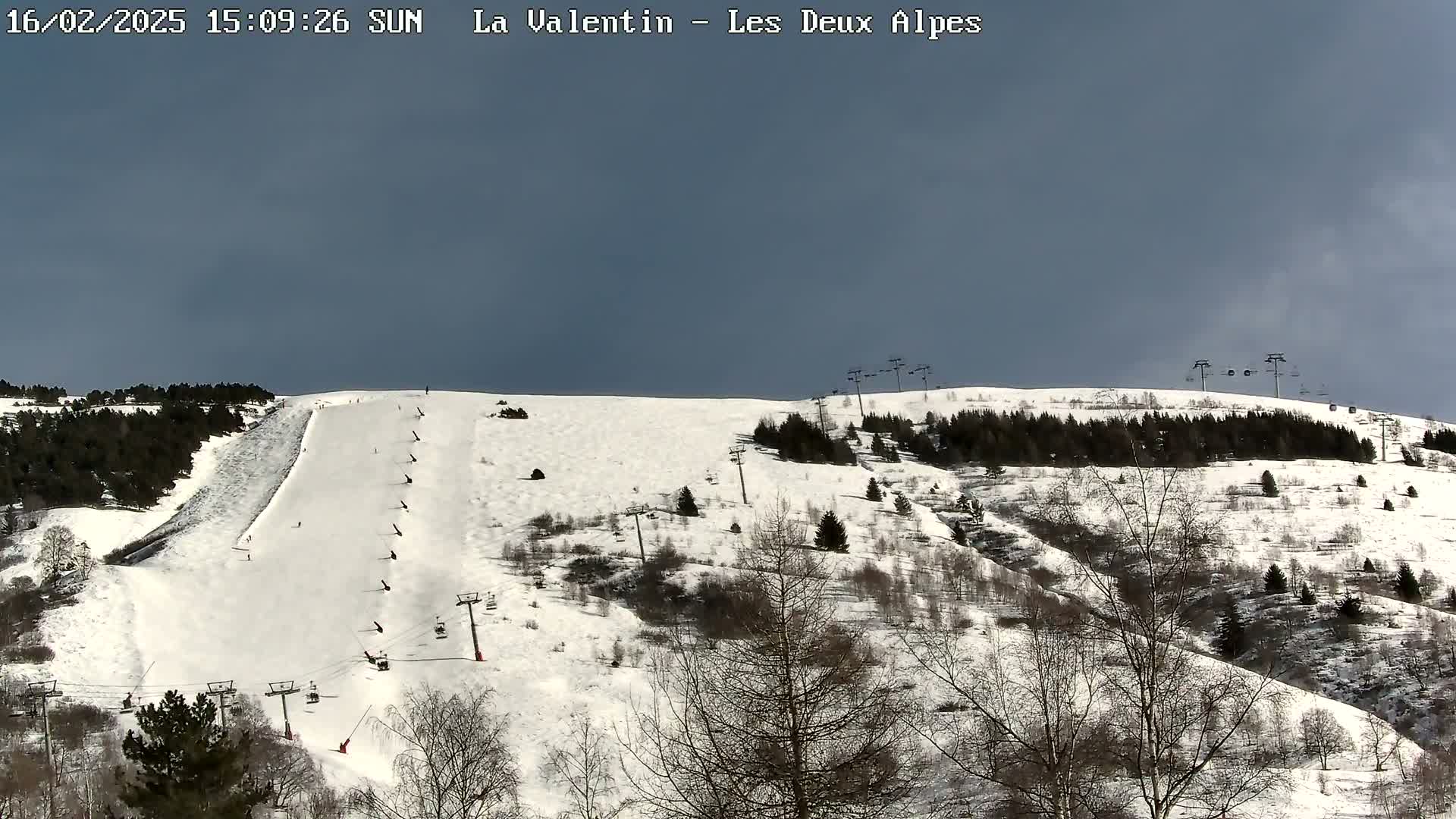 A snow-covered ski slope with several ski lifts and sparsely populated trees under a mostly cloudy sky.