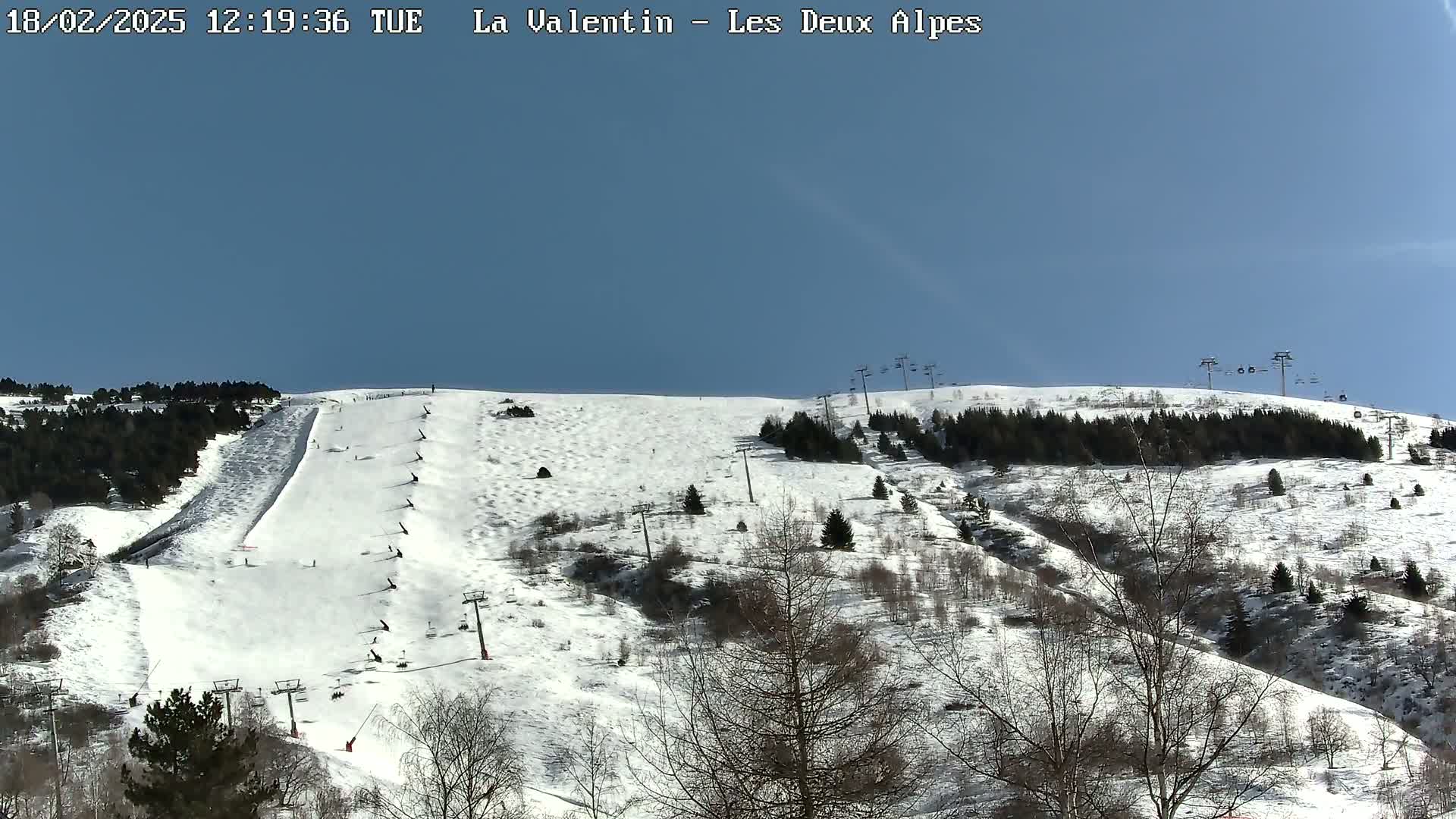 A snow-covered ski slope with several skiers and chairlifts is visible under a clear blue sky.