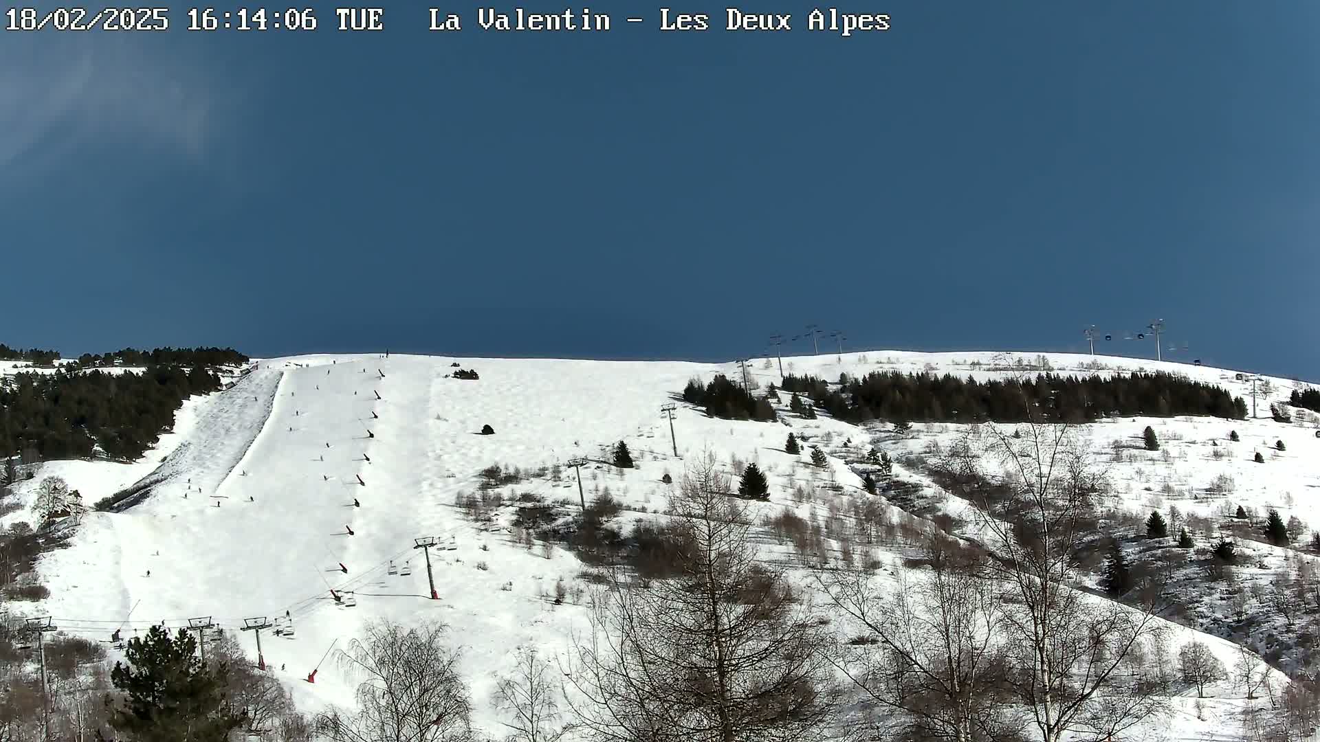 A snow-covered ski slope with several skiers and ski lifts under a clear blue sky.