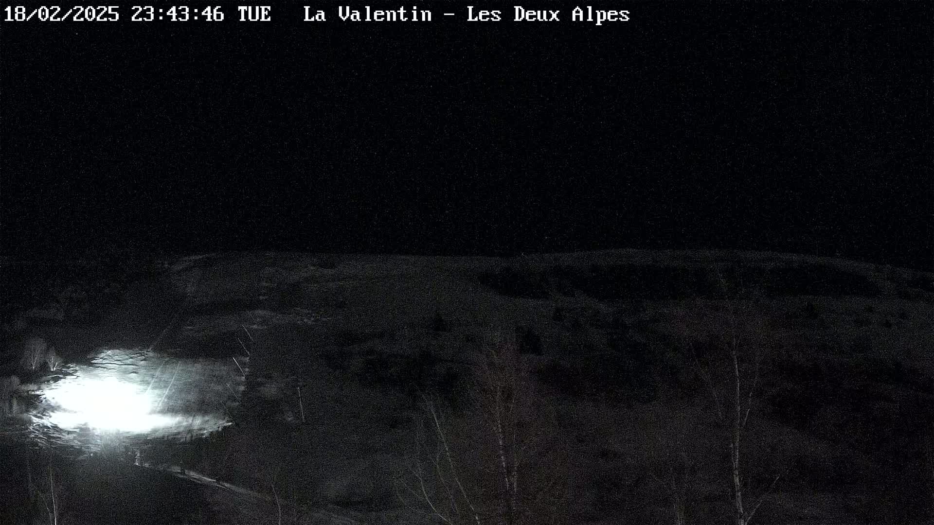 A nighttime, snowy landscape is illuminated by a bright light source in the lower left corner.