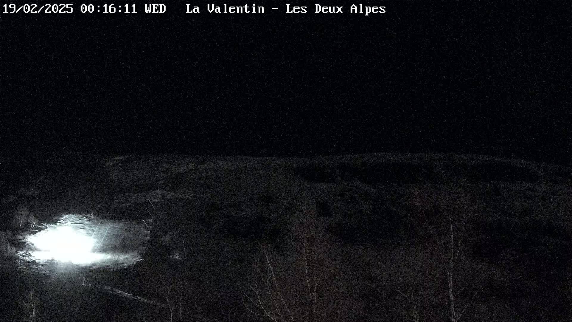 A nighttime, snow-covered landscape is illuminated by a bright light source in the foreground.