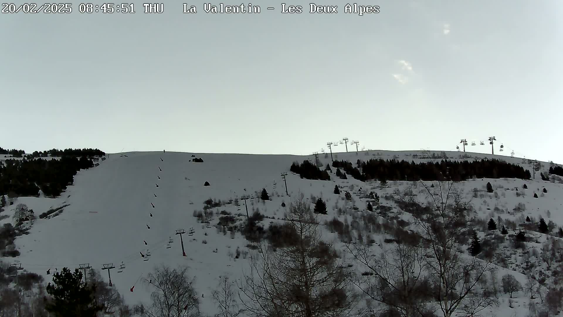 A snow-covered ski slope with several chairlifts and sparsely wooded areas under a pale sky.