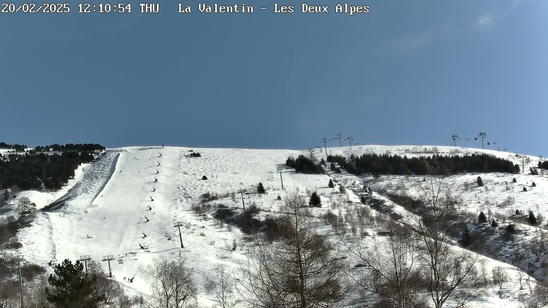 A snow-covered ski slope with several skiers visible, under a clear blue sky.