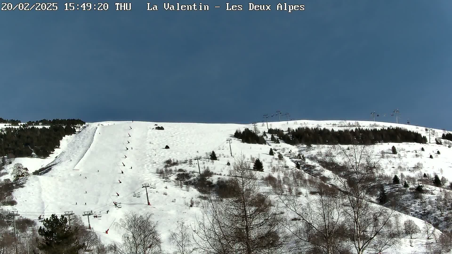 A snow-covered ski slope with skiers and ski lifts under a clear blue sky.