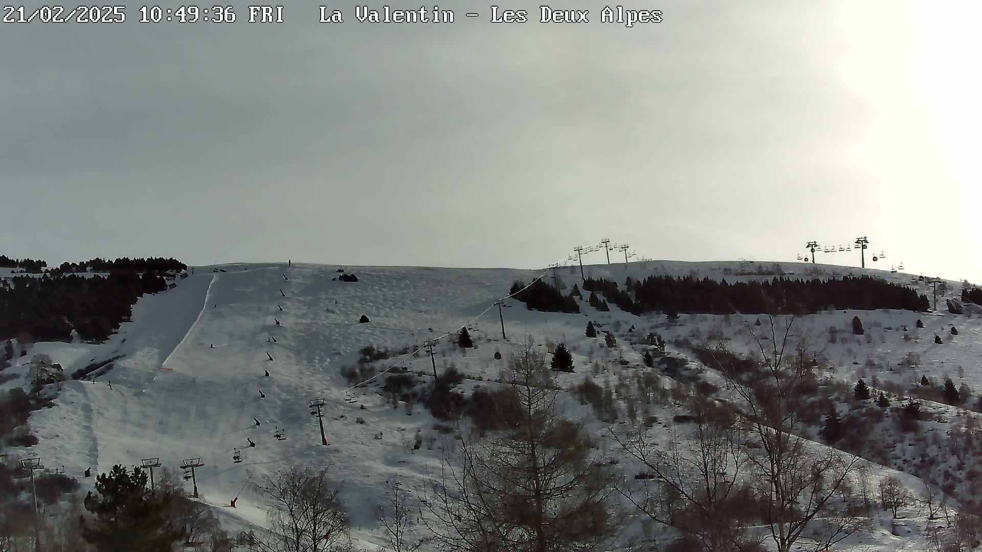 A snowy ski slope with several chairlifts and skiers visible under a mostly cloudy sky.