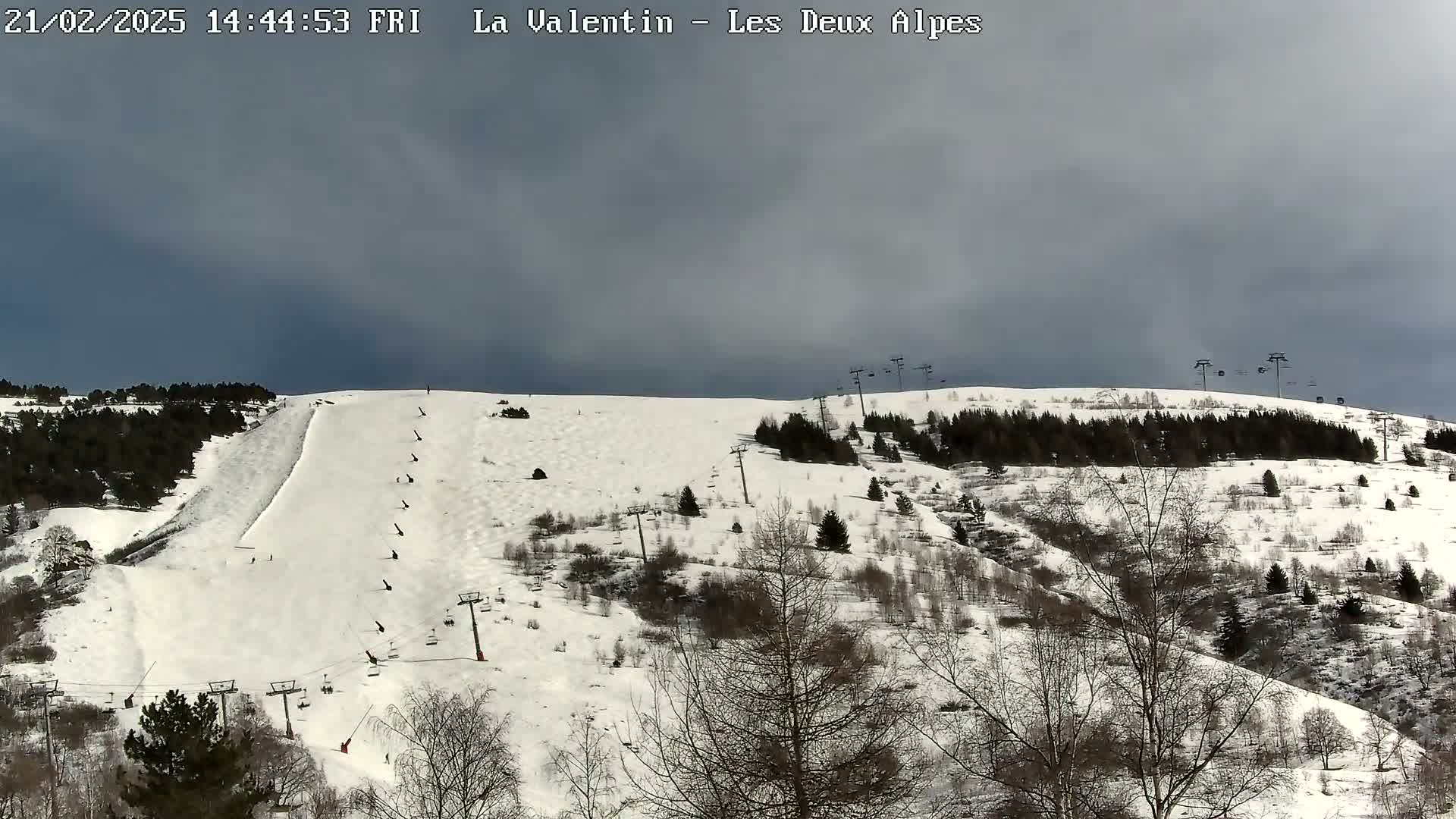 A snow-covered ski slope with several ski lifts and sparsely wooded areas under a cloudy sky.