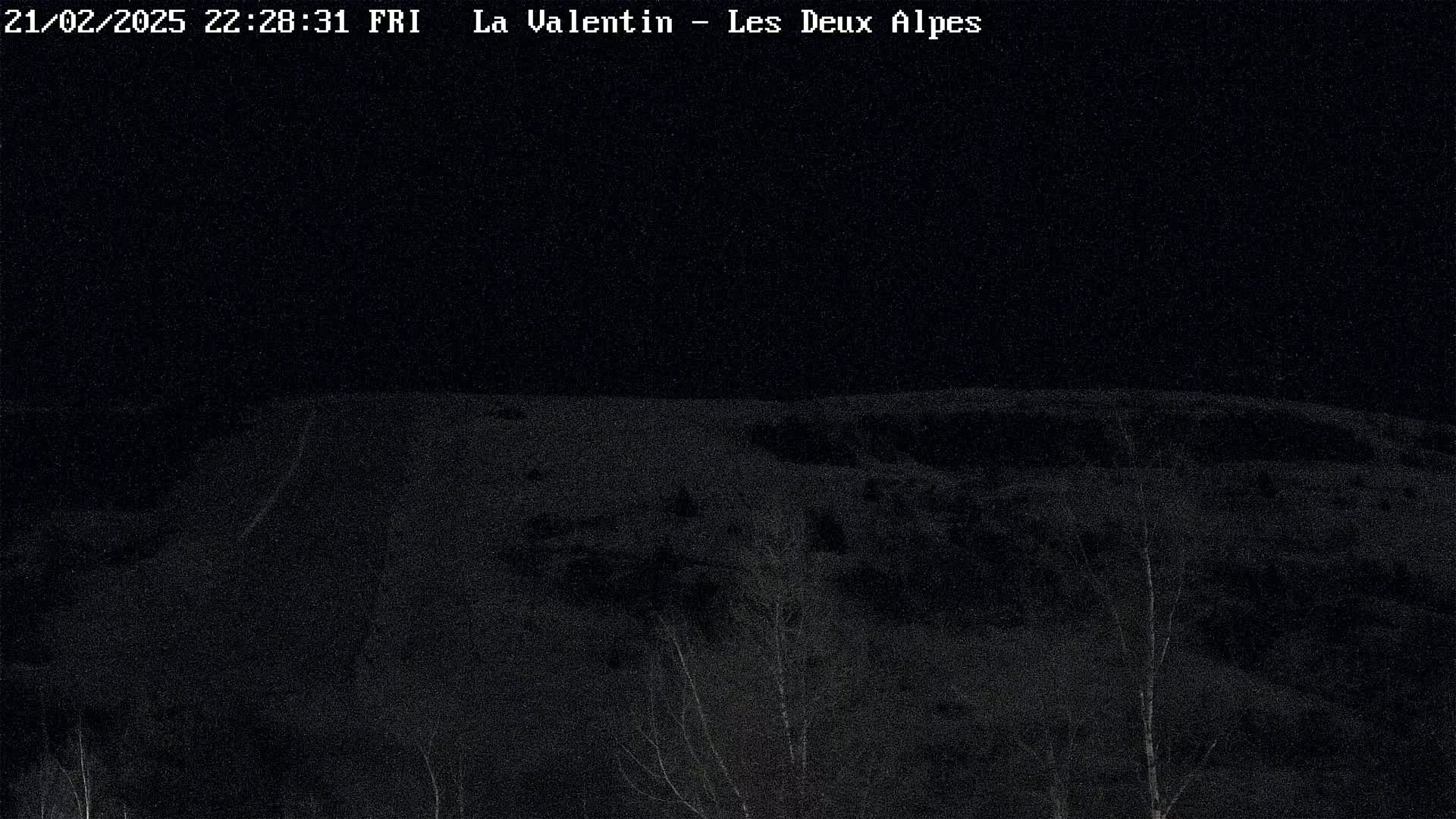 A nighttime, snow-covered landscape is visible, showing a hilly terrain with sparse, dark trees under a dark sky.