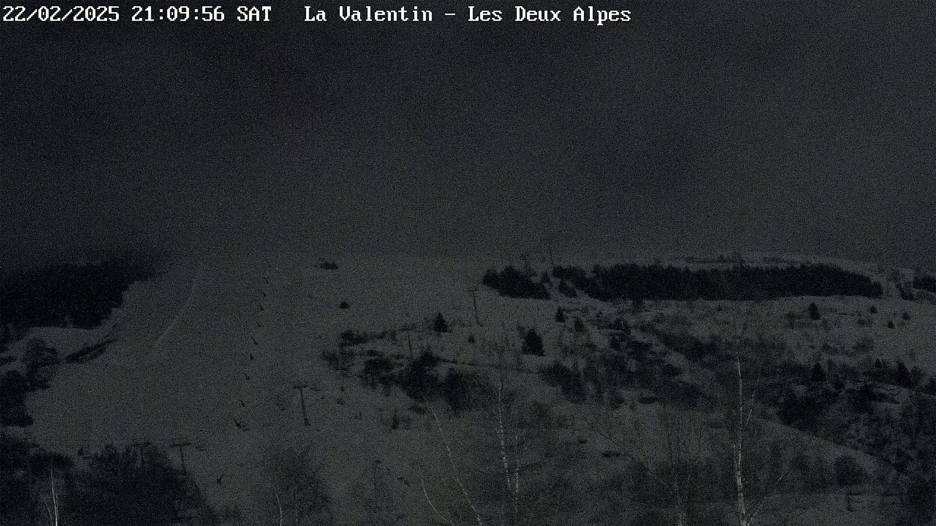 A nighttime view of a snow-covered ski slope with sparse trees and ski lifts under a dark sky.
