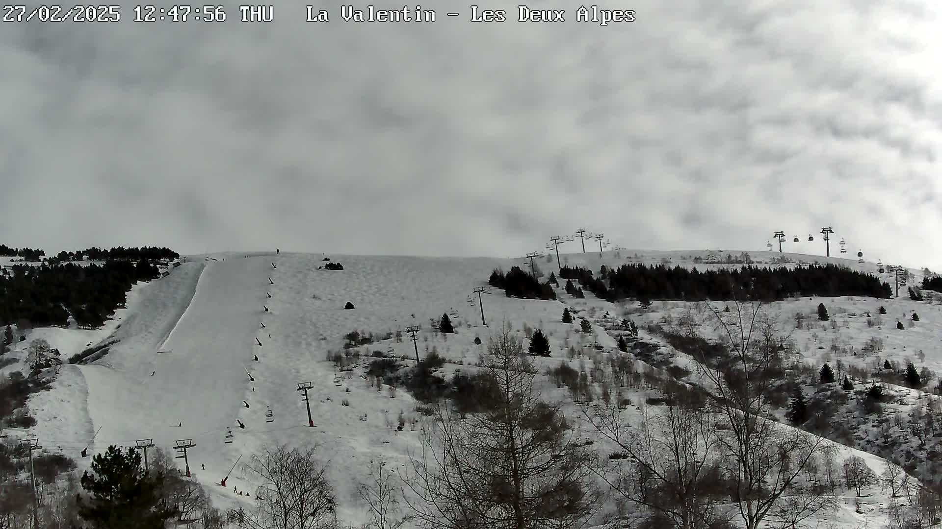 A snow-covered ski slope with several chairlifts and sparsely wooded areas under an overcast sky.
