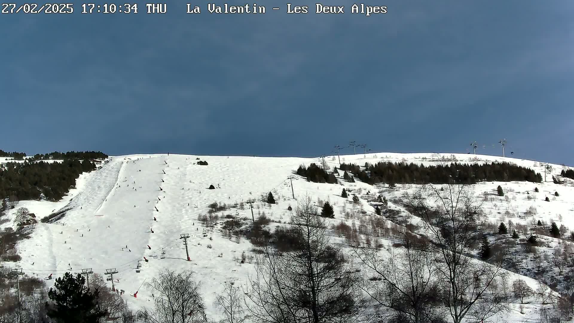 A snow-covered ski slope with sparsely wooded areas and several ski lifts under a clear blue sky.