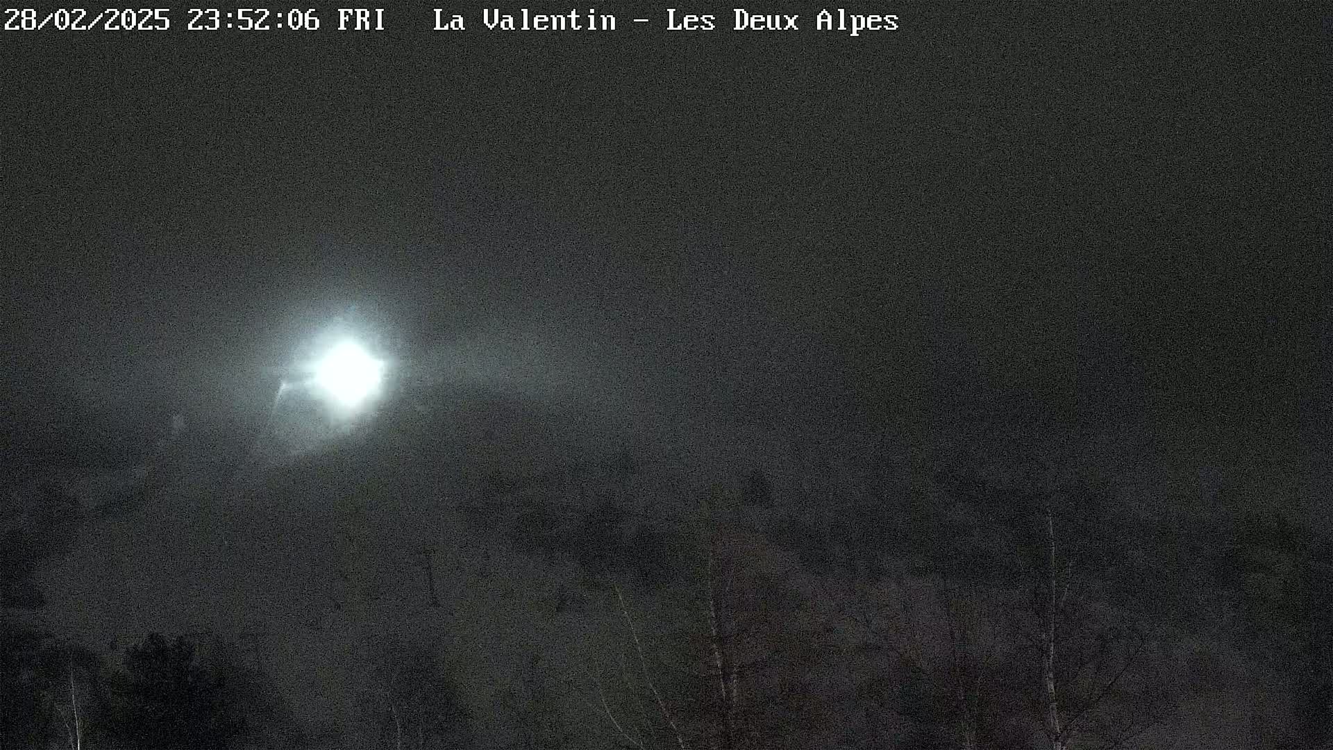 A bright moon shines over a dark, snow-covered landscape at night.