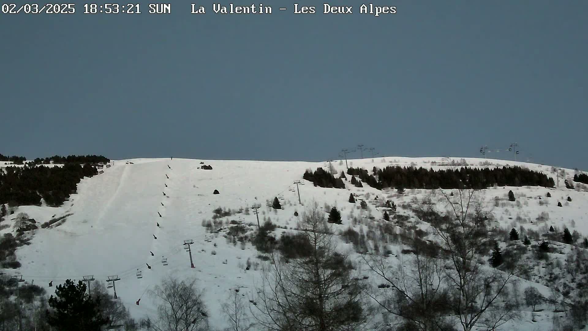 A snow-covered ski slope with sparsely wooded areas and several ski lifts under a clear, light-blue sky.
