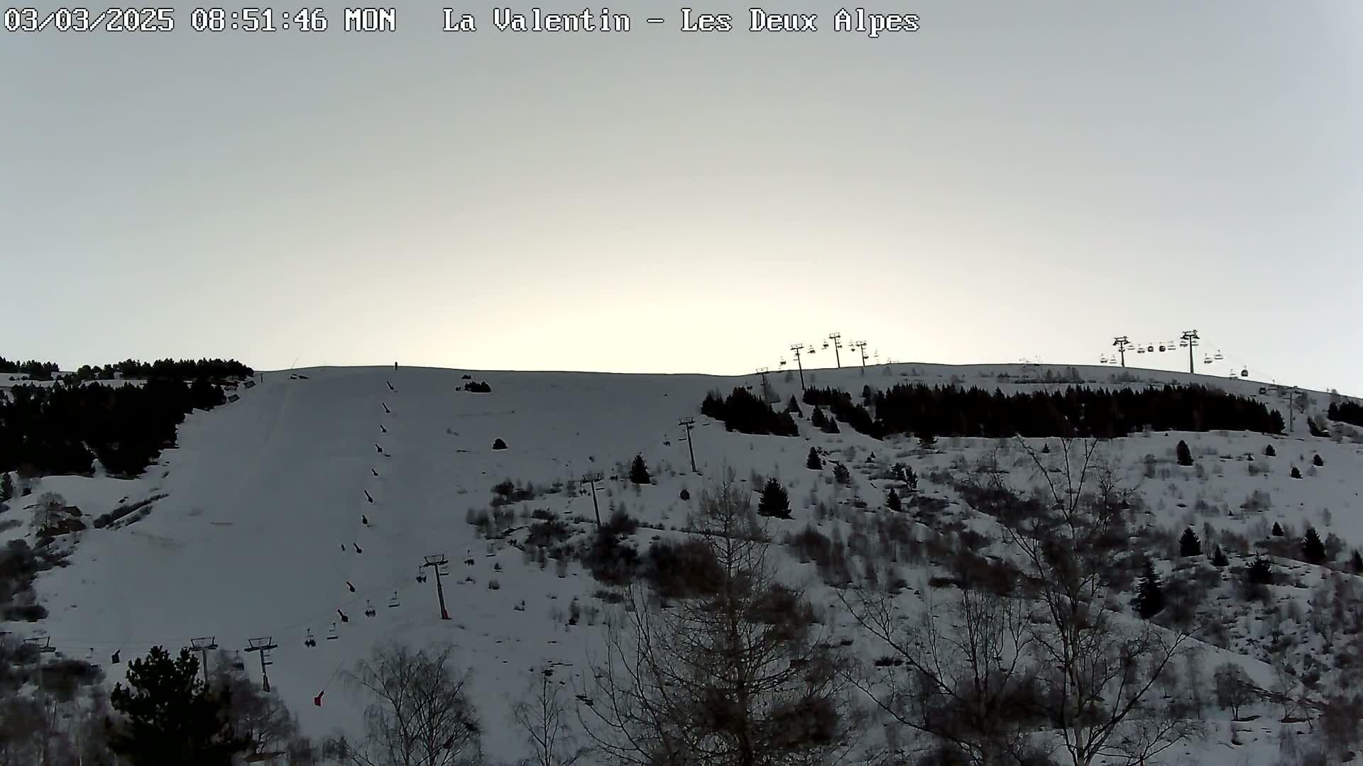 A snow-covered ski slope with several chairlifts visible under a pale, overcast sky.
