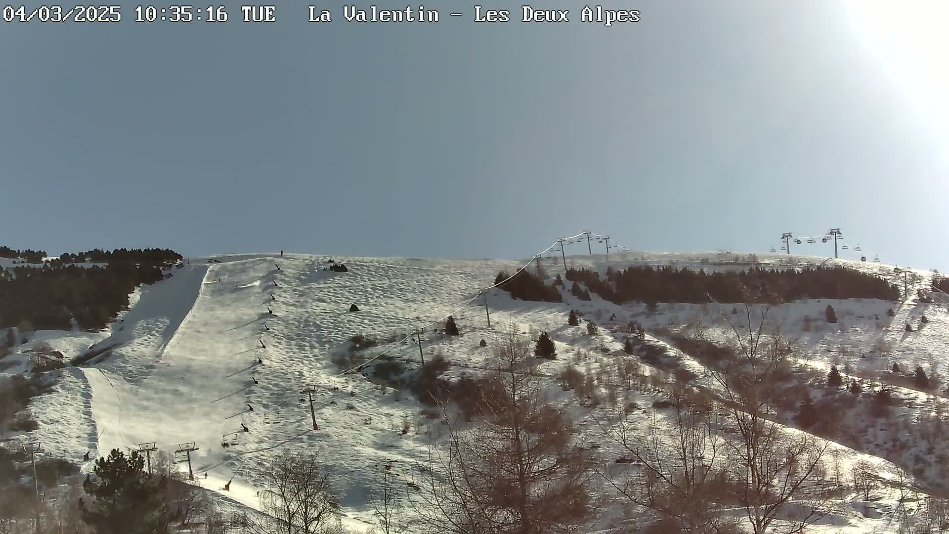 A sunny day on a snow-covered ski slope with several chairlifts and skiers visible.