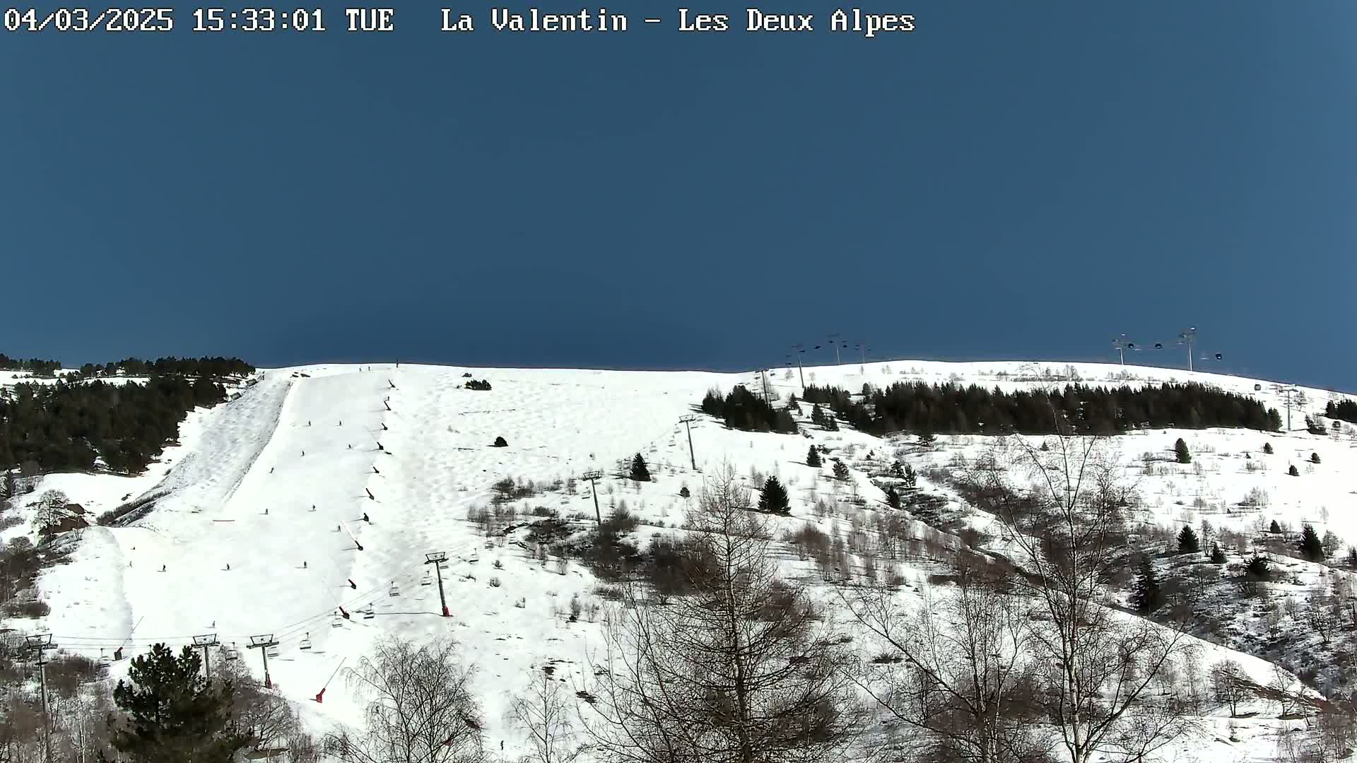 A snow-covered ski slope with several skiers visible under a clear blue sky.