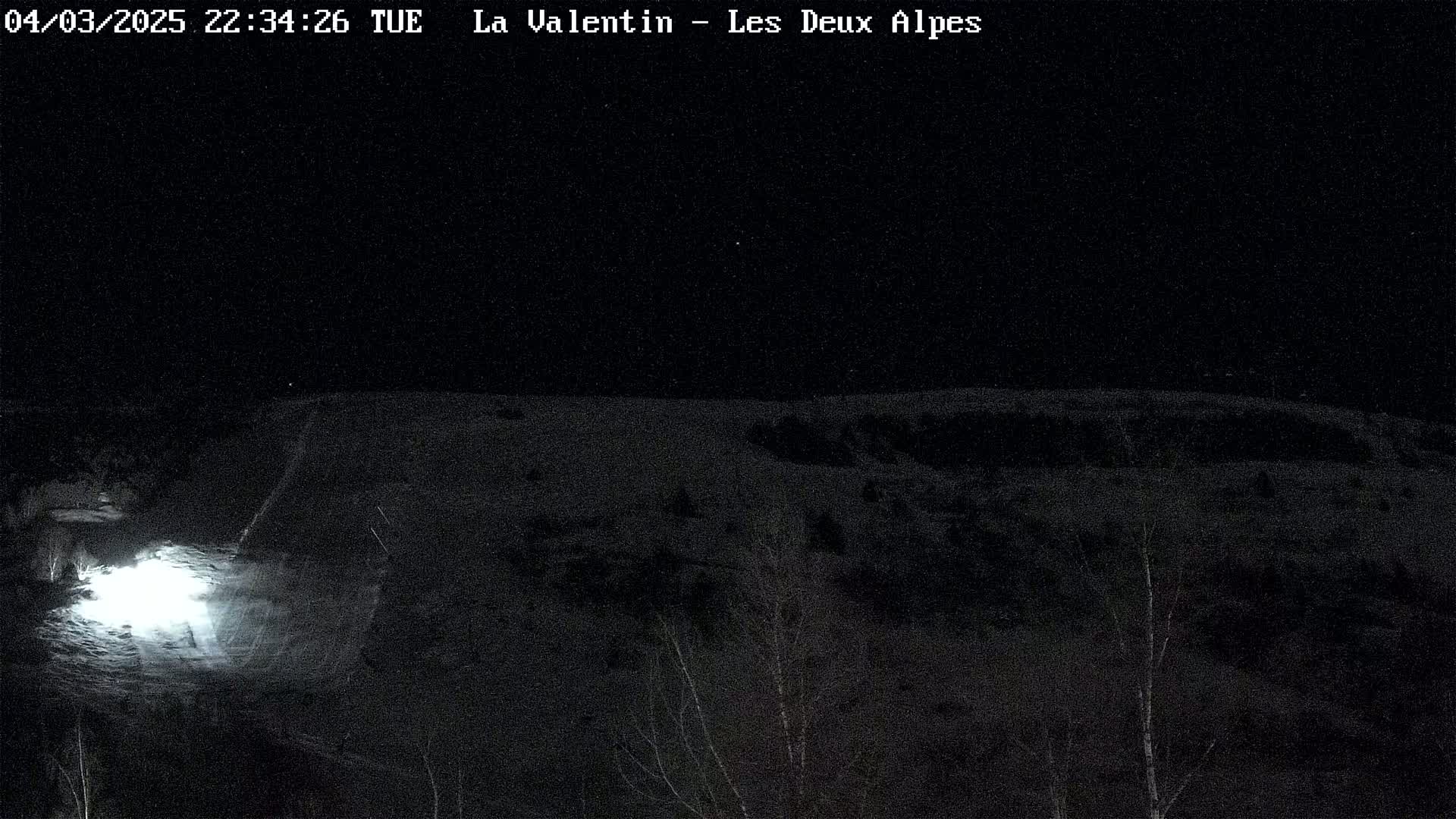 A nighttime, snow-covered landscape is illuminated by a bright light source in the foreground under a dark sky.