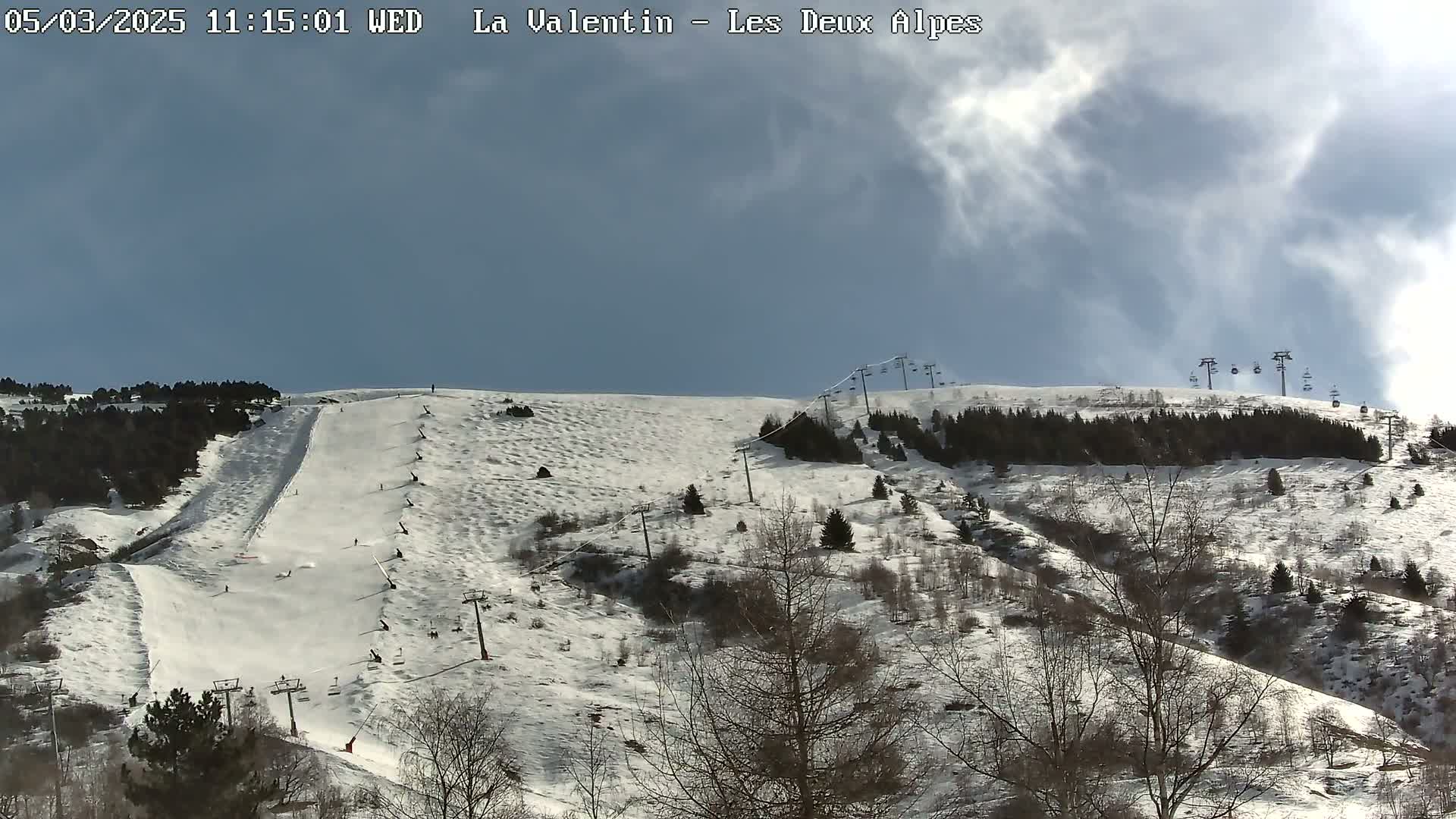 A snow-covered ski slope with several skiers and chairlifts is visible under a partly cloudy sky.