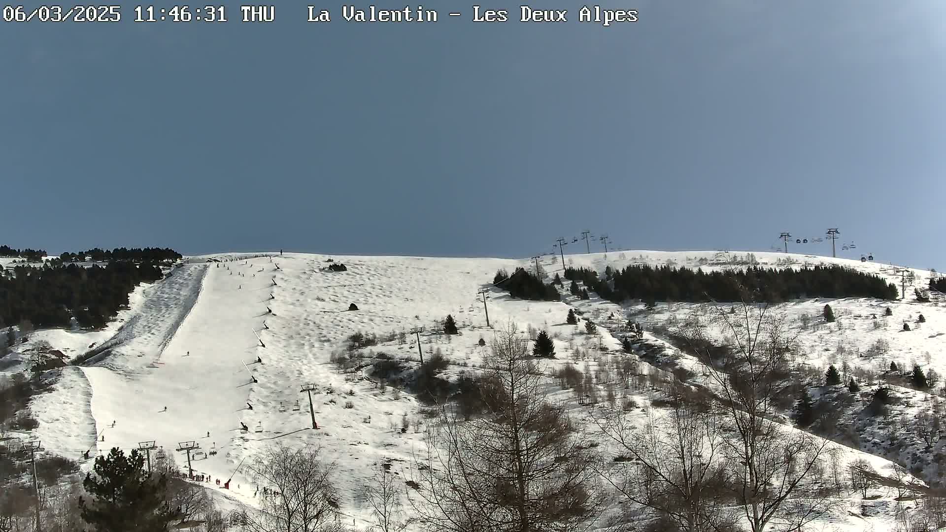 A snow-covered ski slope with several skiers and ski lifts under a clear blue sky.