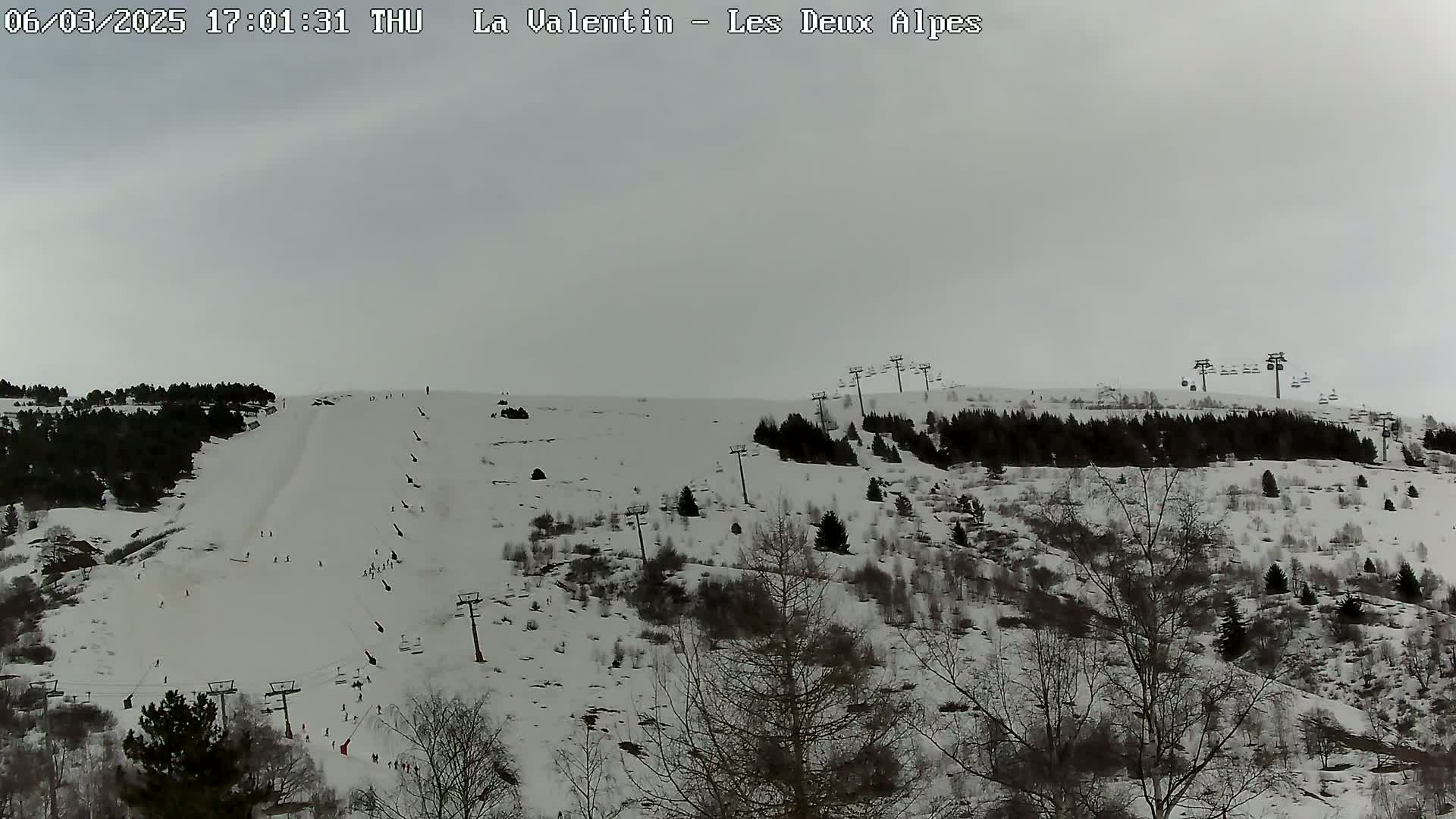 A snow-covered ski slope with several skiers and ski lifts is visible under an overcast sky.
