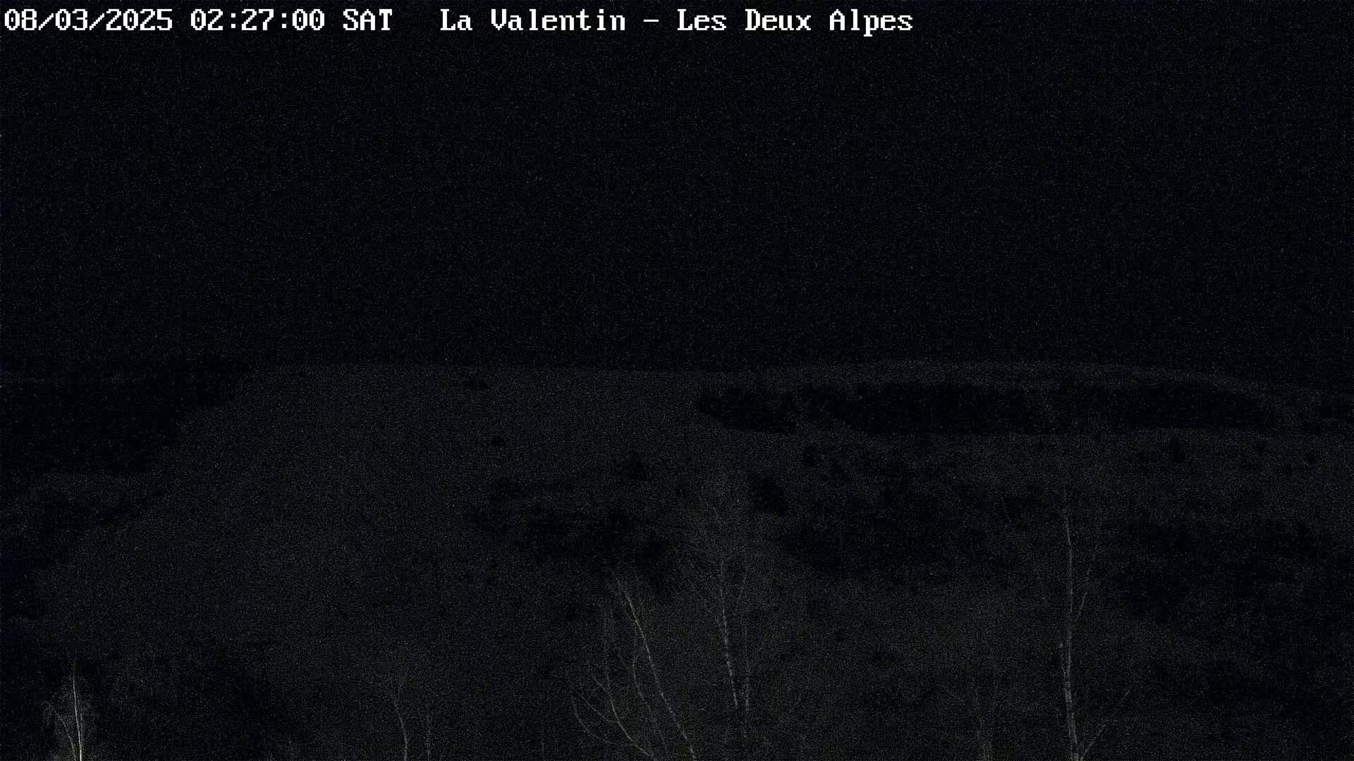 A nighttime, dark, snowy landscape is visible, with some bare trees and a mostly flat, snow-covered area extending into the distance.