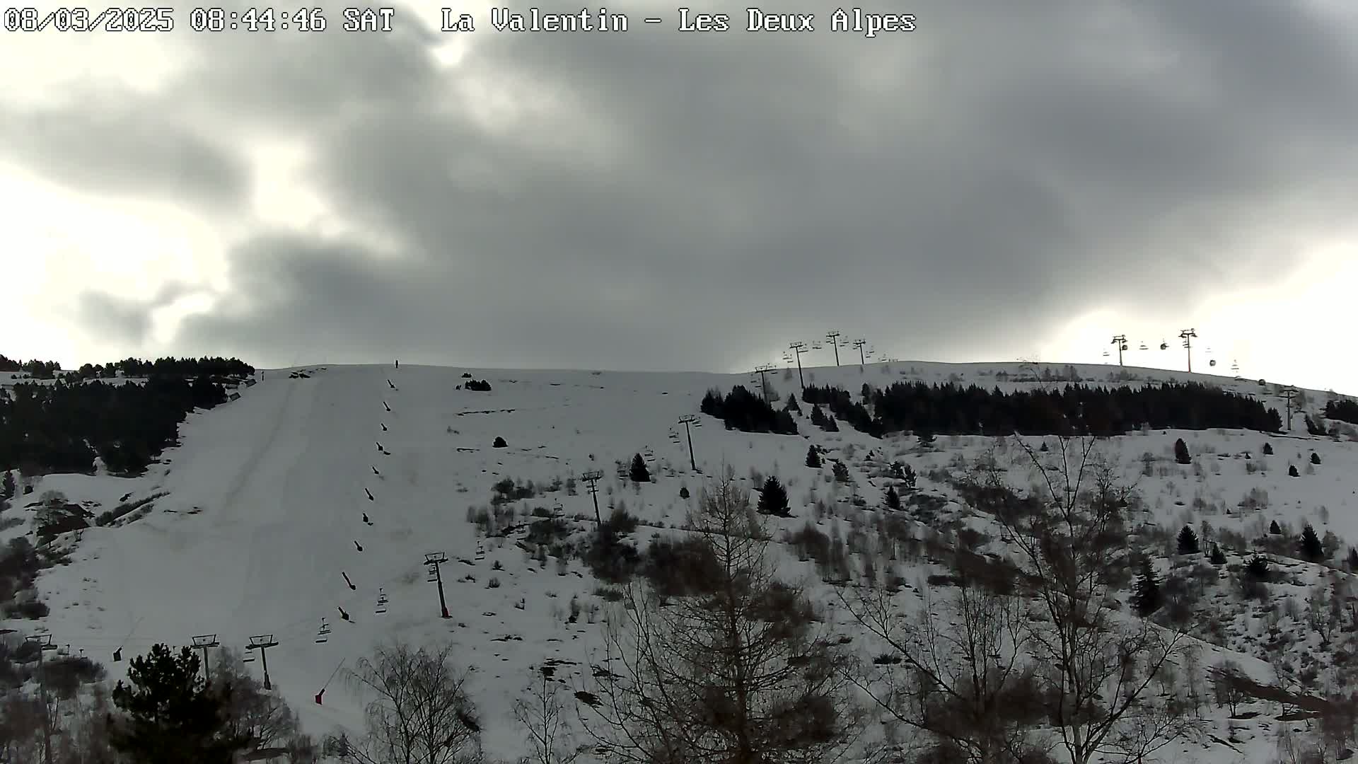 A snow-covered ski slope with several ski lifts is visible under a cloudy sky.