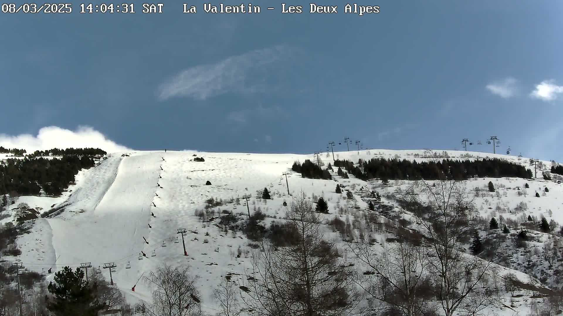 A snow-covered ski slope with sparsely wooded areas and several ski lifts under a mostly clear blue sky.