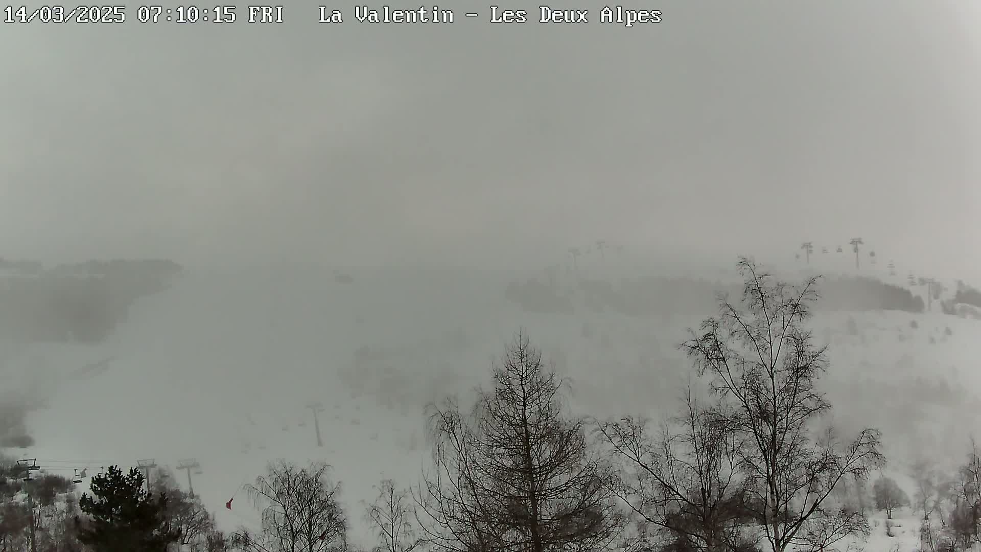 A snow-covered landscape is obscured by heavy fog or blowing snow, with bare trees and ski lifts faintly visible in the distance.