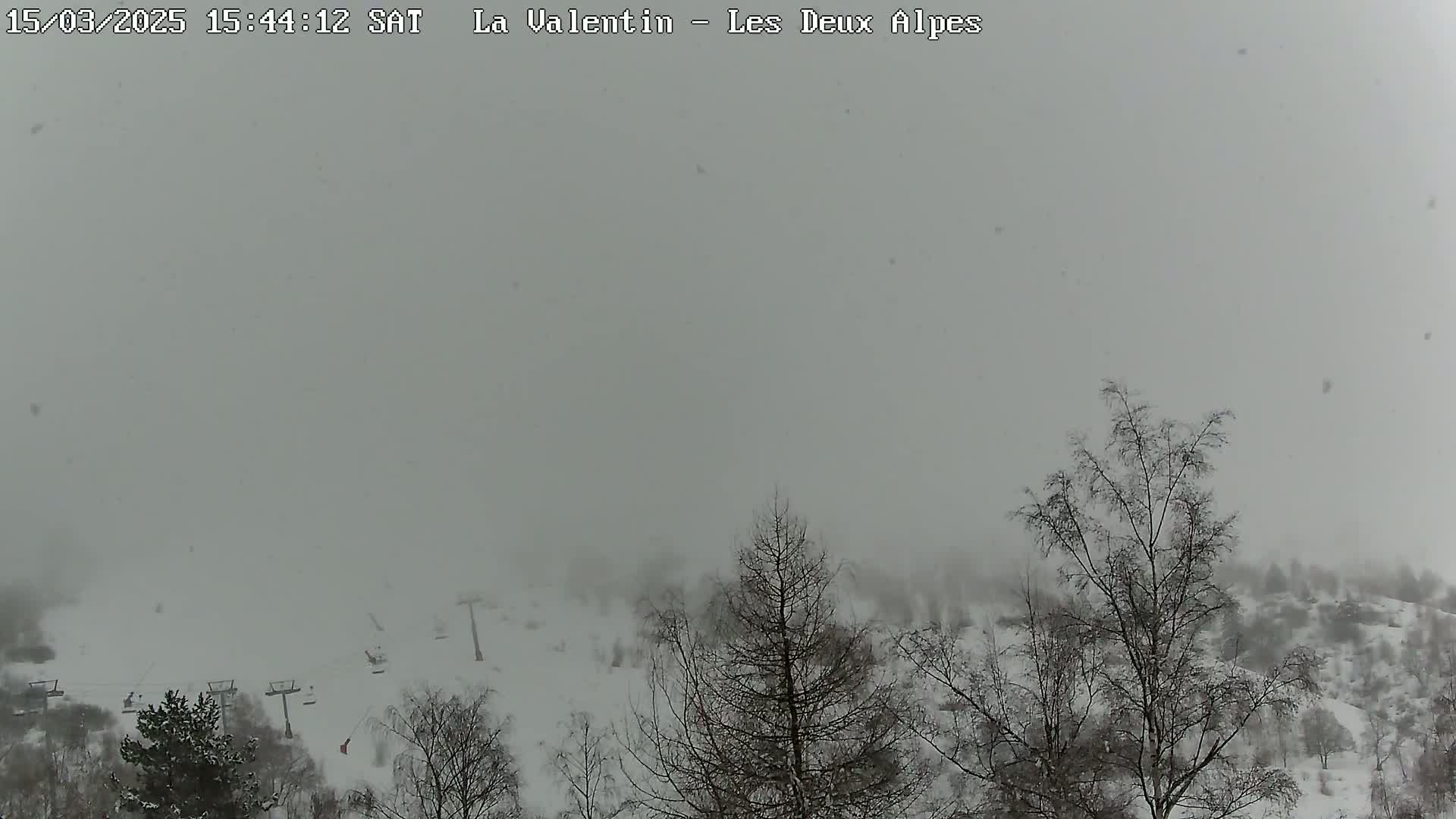 A snowy, foggy landscape with bare trees and ski lifts is visible through falling snow.