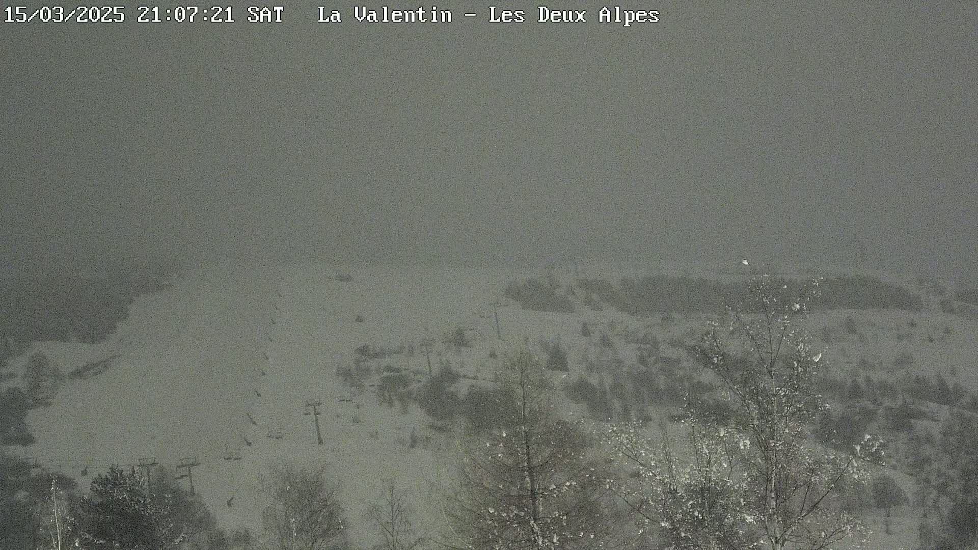 A snow-covered ski slope with sparsely-treed areas is seen in heavy snowfall.